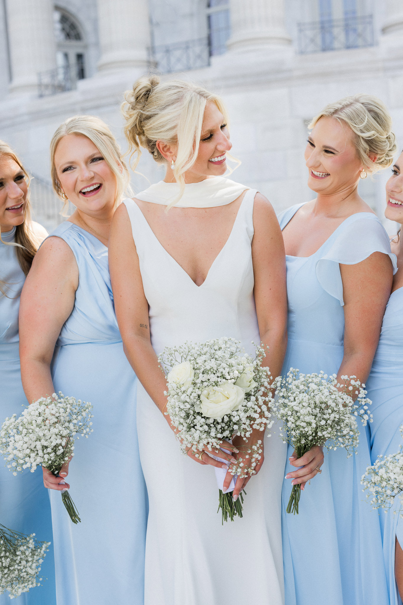 Candid moment of the bride smiling with her bridesmaids, showing off their pastel blue dresses and cheerful energy.