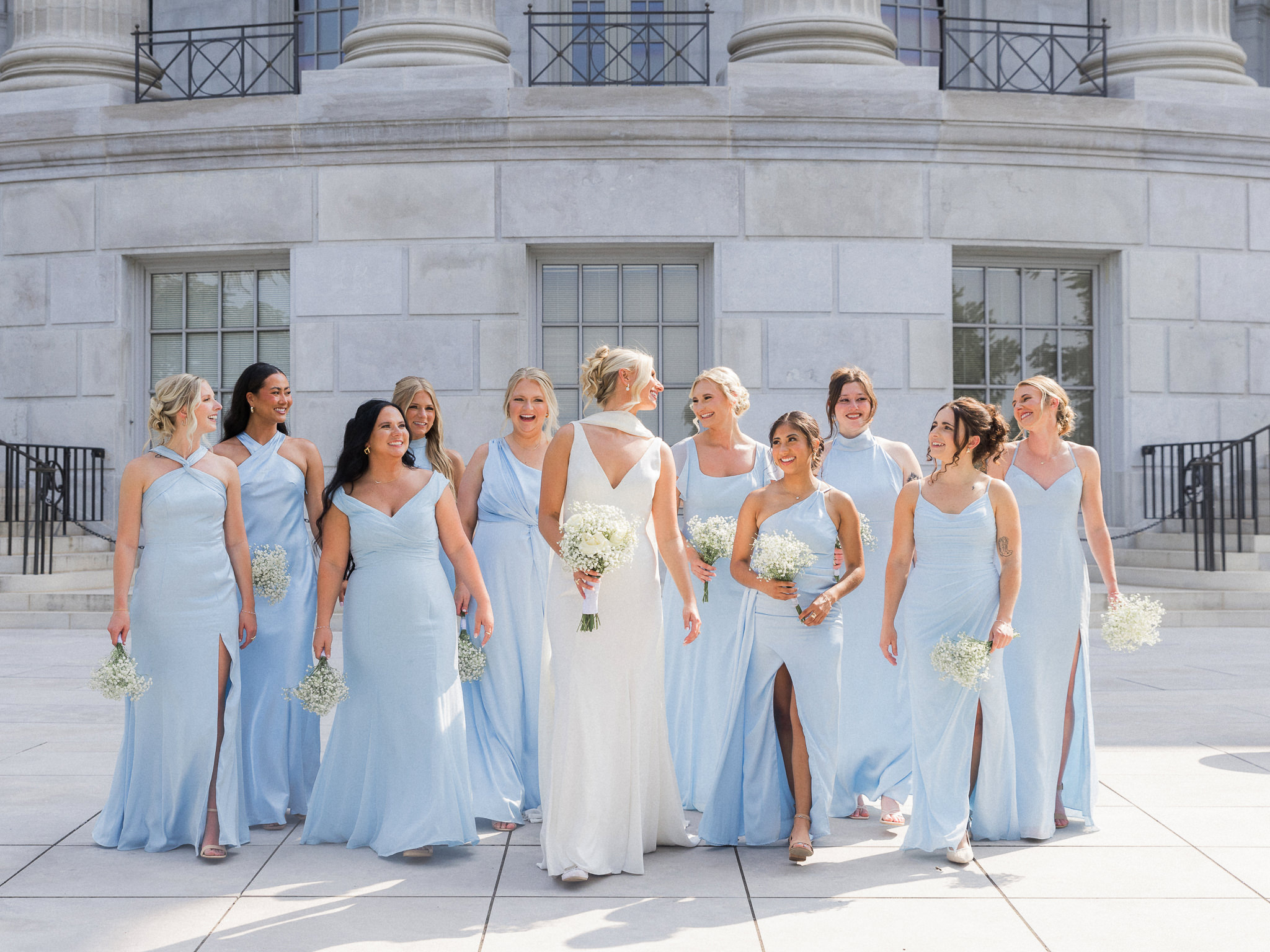 Joyful bride and bridesmaids walk in front of a white-columned building, capturing the celebration.