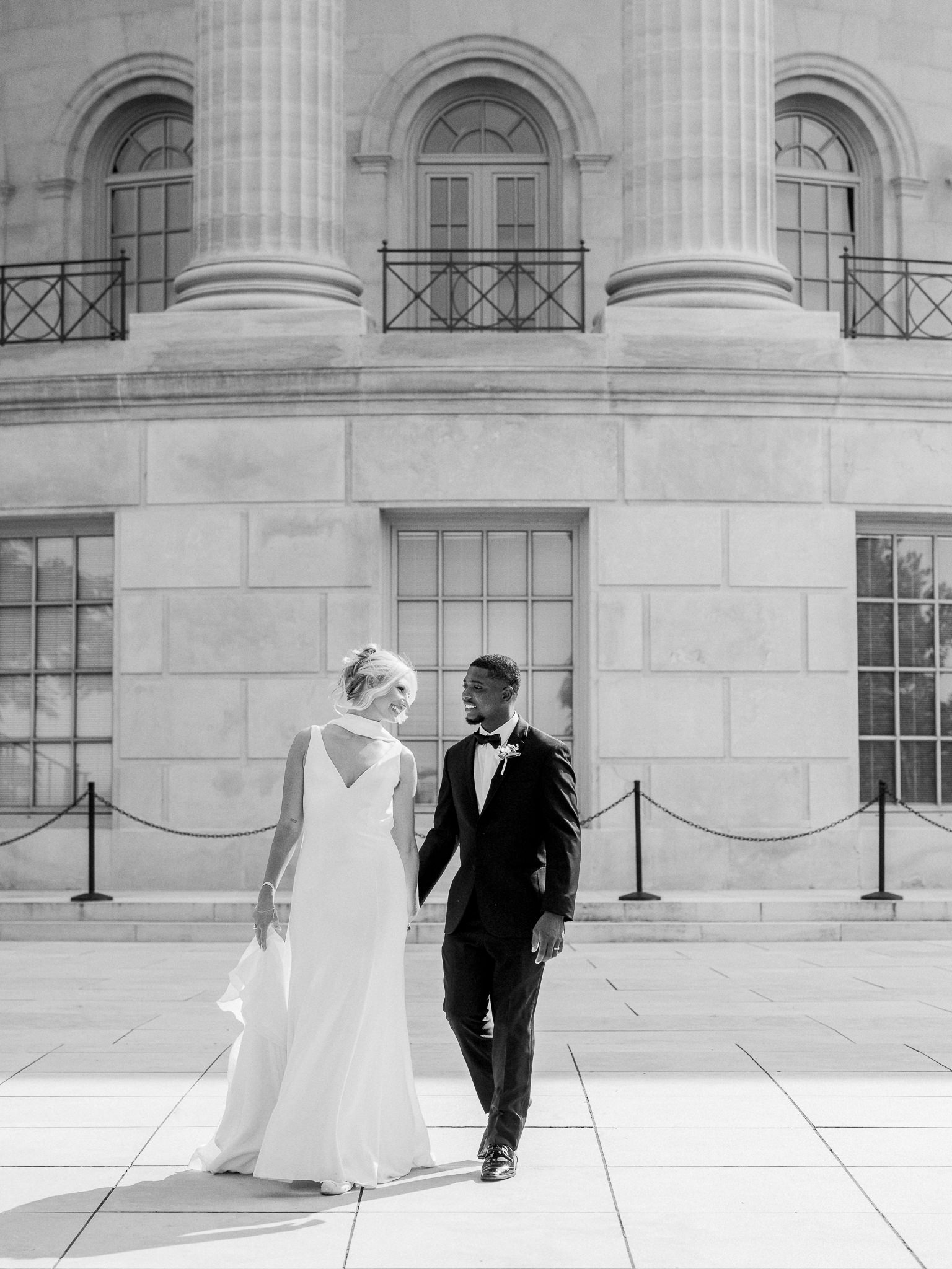 ride and groom walk hand in hand, gazing at each other in front of a grand courthouse — timeless moment by Missouri wedding photographer.