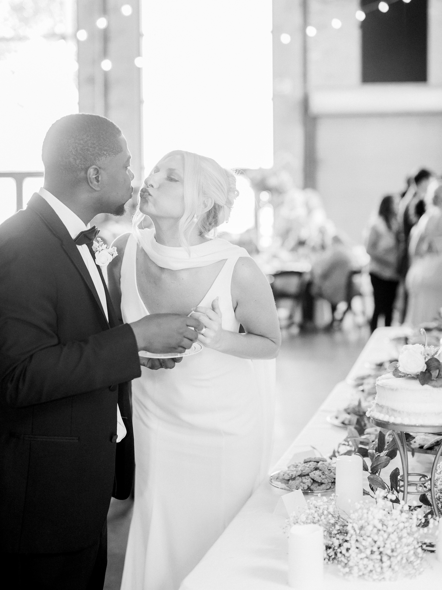 Bride and groom kiss by the dessert table during their wedding reception at an industrial venue in Missouri.