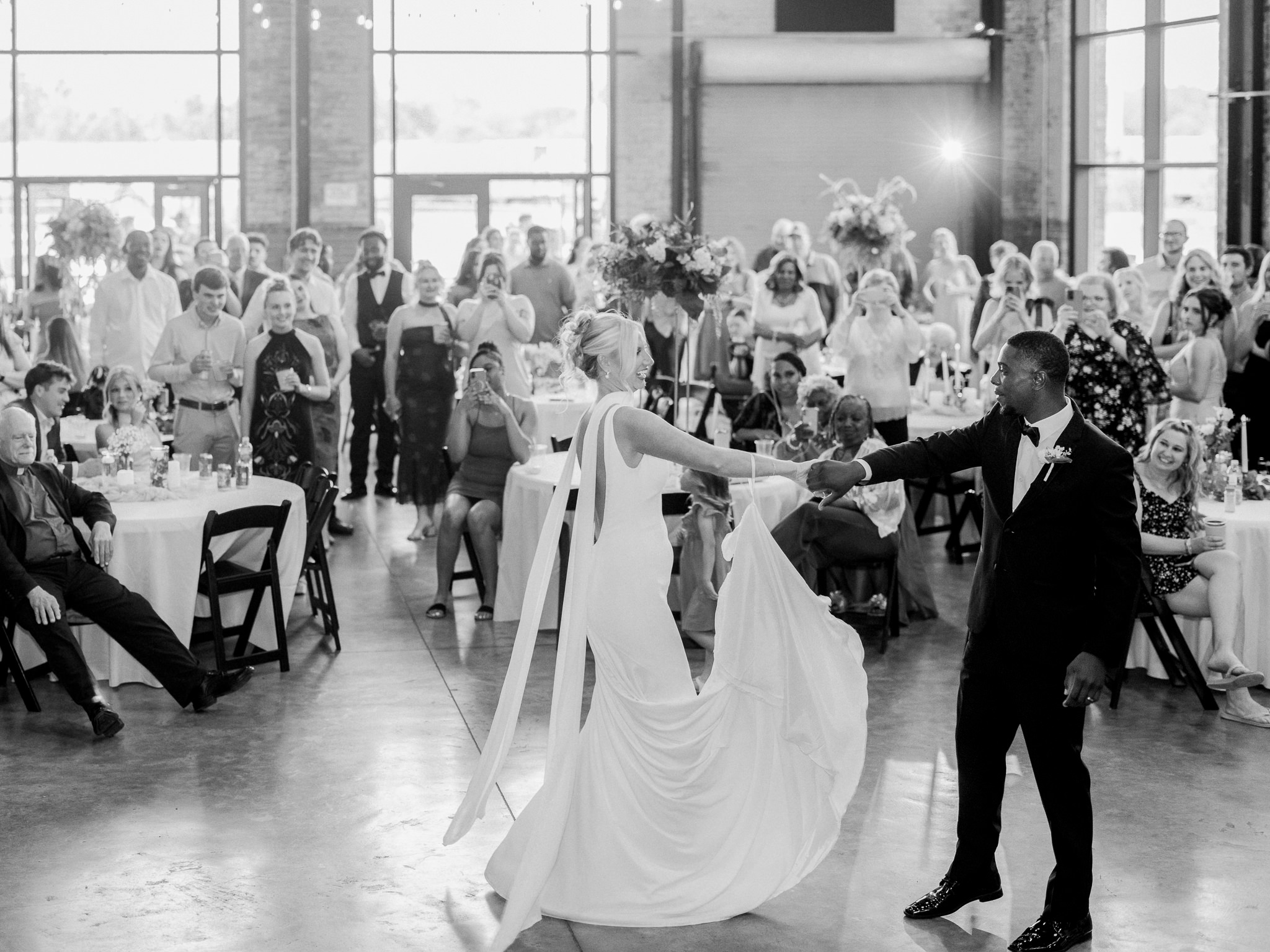 Bride and groom share their first dance surrounded by cheering guests at their reception.