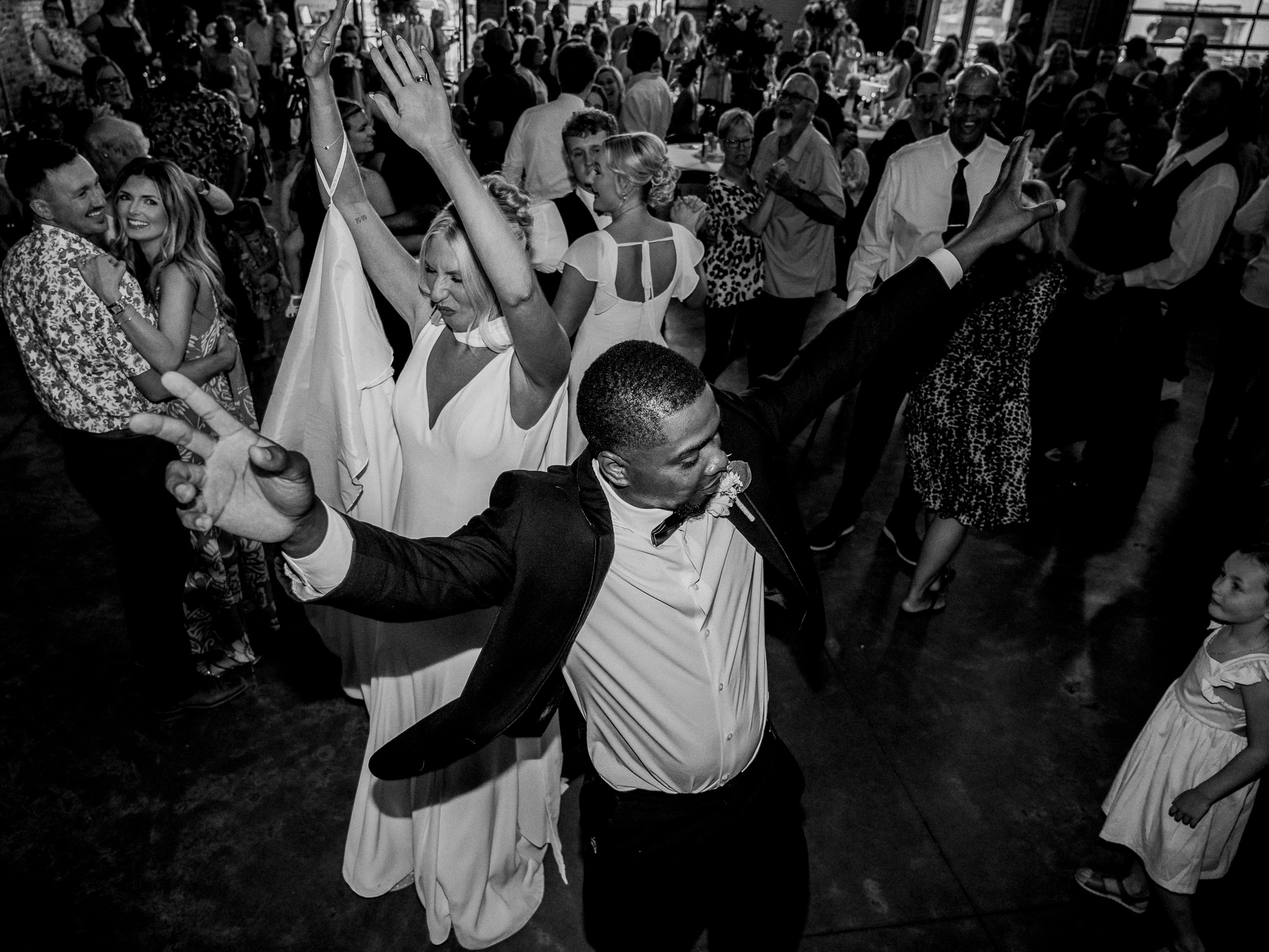 Bride and groom dance with arms raised during a packed and lively wedding reception.