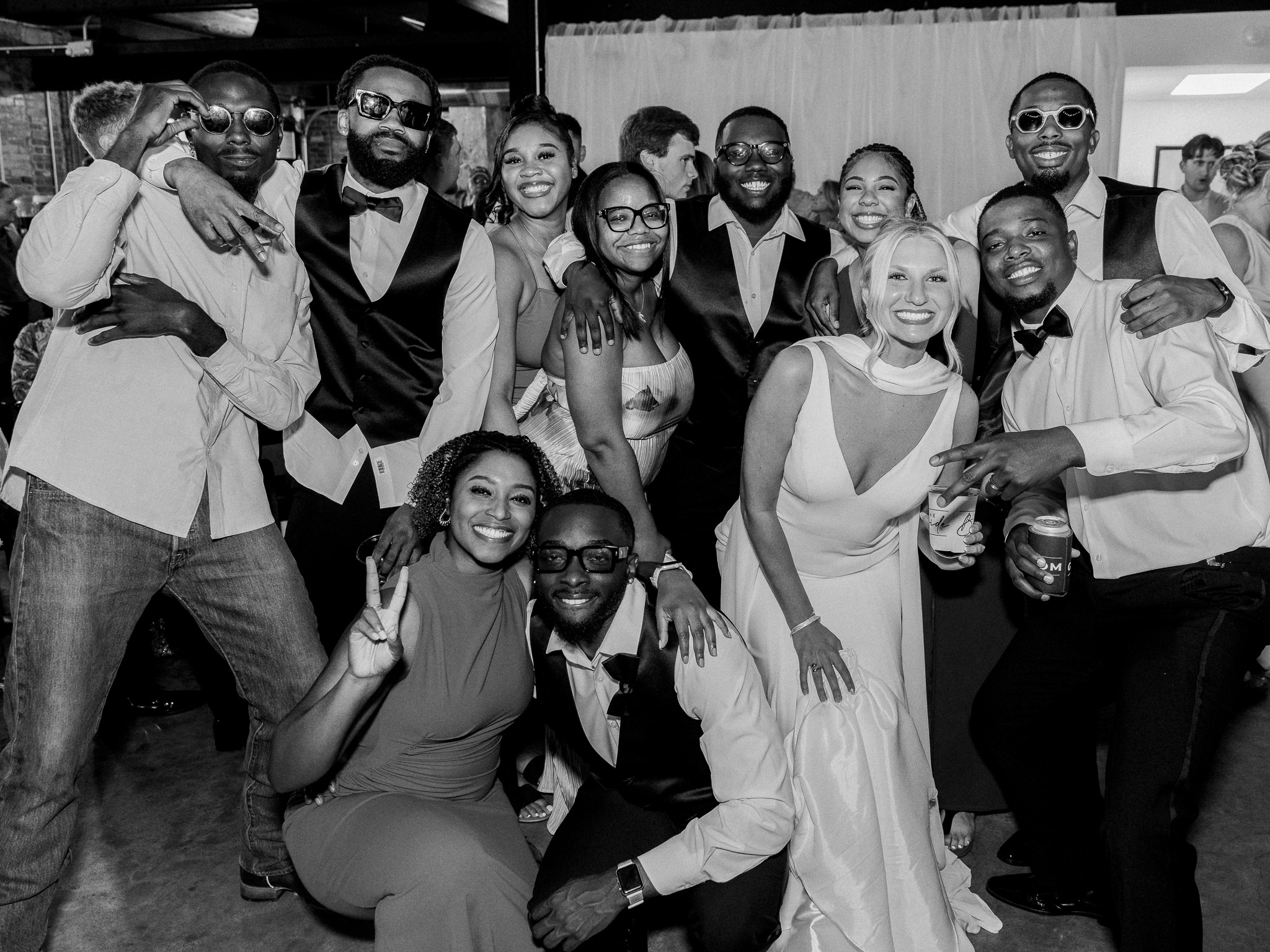 Bride and groom pose for a fun group photo with their wedding party and friends.
