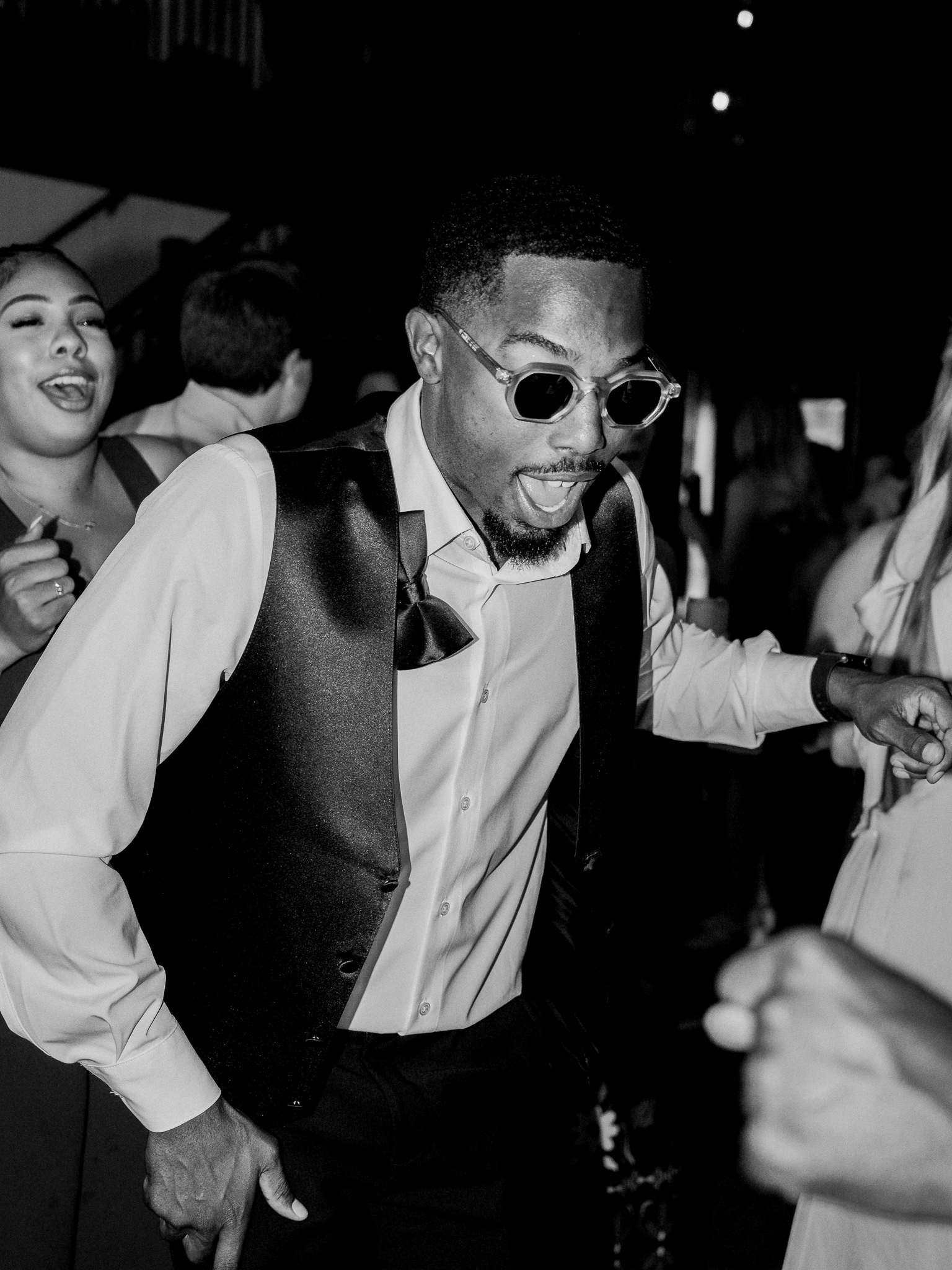 Groom dances in sunglasses and vest, enjoying the reception party atmosphere.