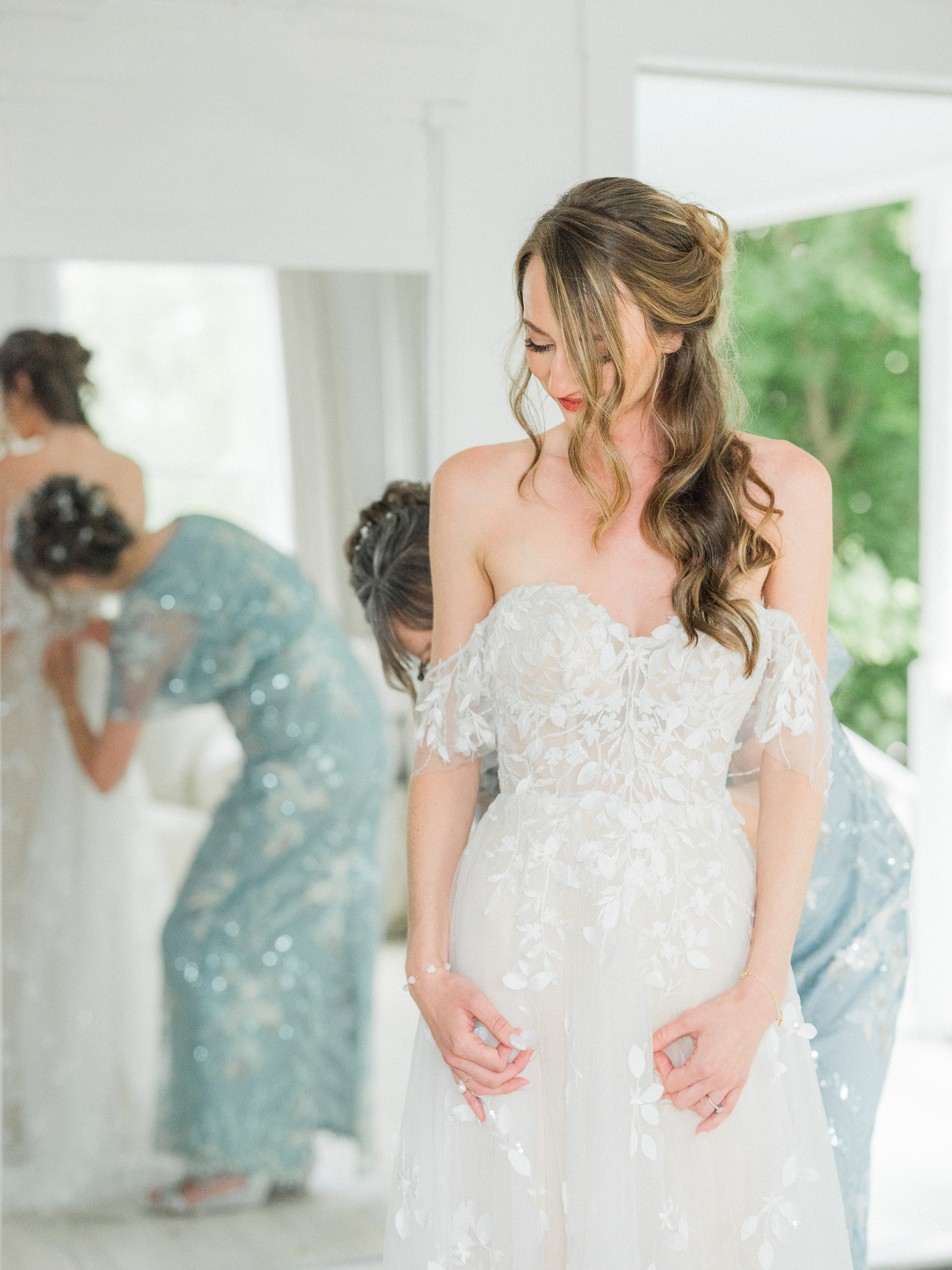 Candid moment of the bride being helped into her gown by her mom, reflected in a full-length mirror.