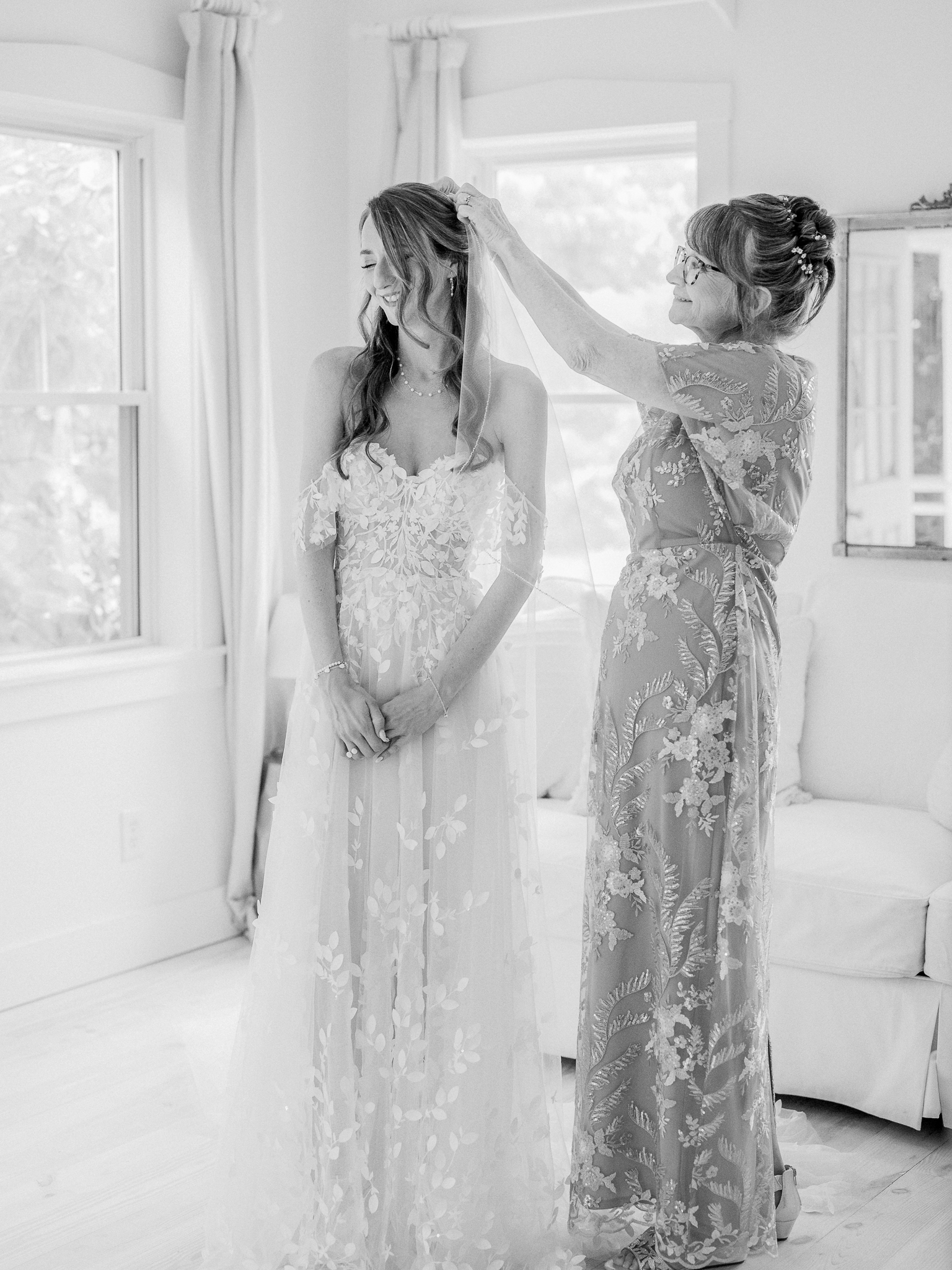 Mother gently places veil on bride’s head in a sun-drenched room as the bride beams.