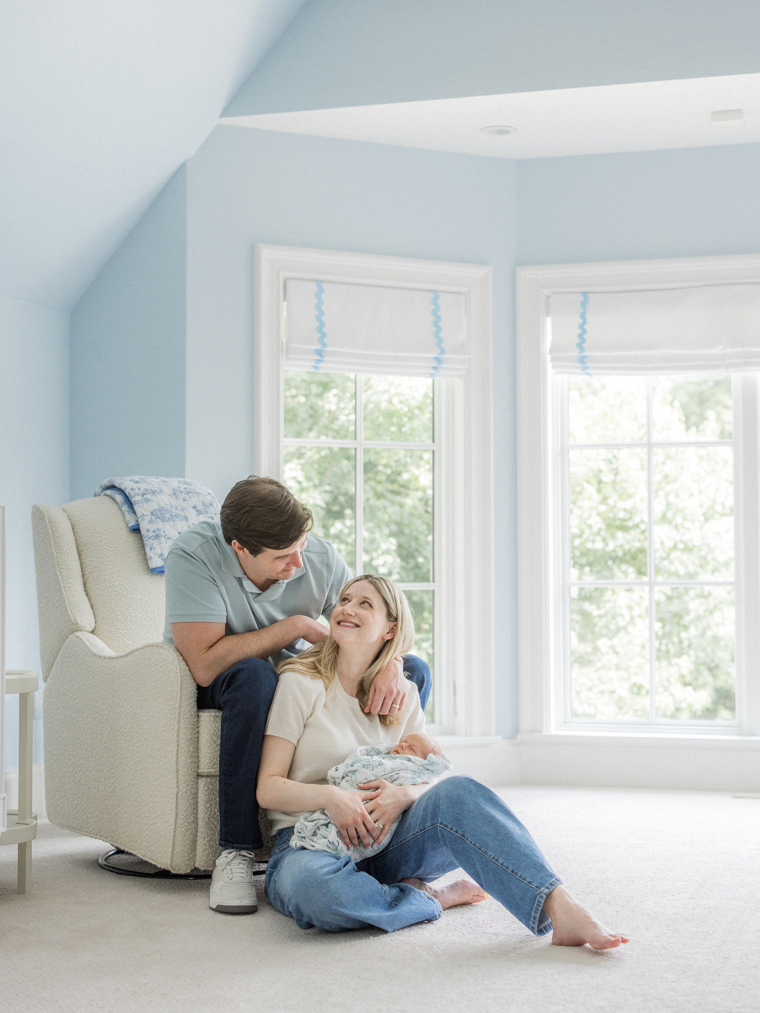 Parents sitting in a bright nursery, sharing a joyful moment during their Columbia Missouri newborn session.