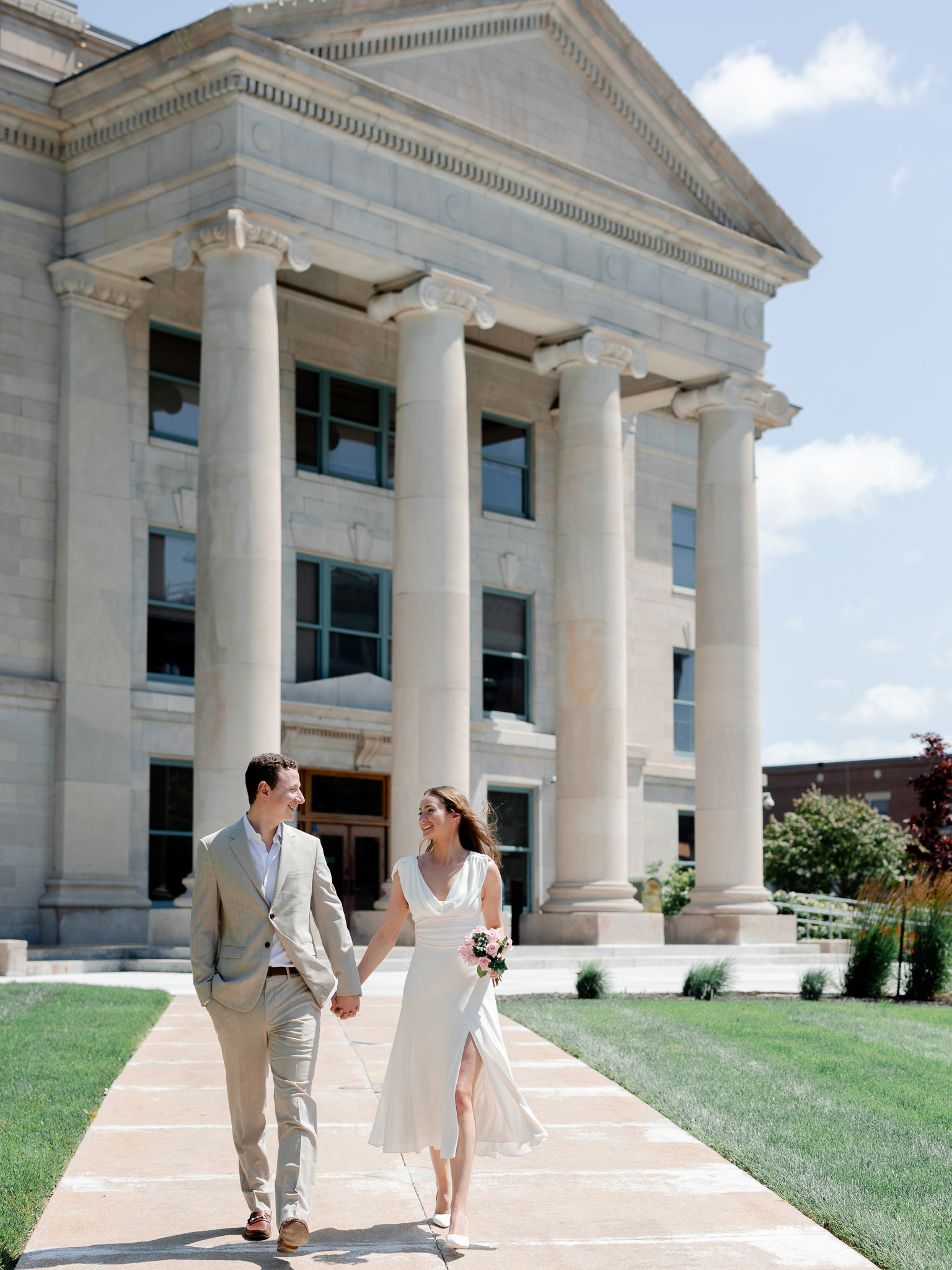 Arthur and Madison holding hands and walking outside the Boone County Courthouse in Columbia Missouri on their wedding day – photographed by Love Tree Studios during their courthouse wedding in Columbia Missouri.