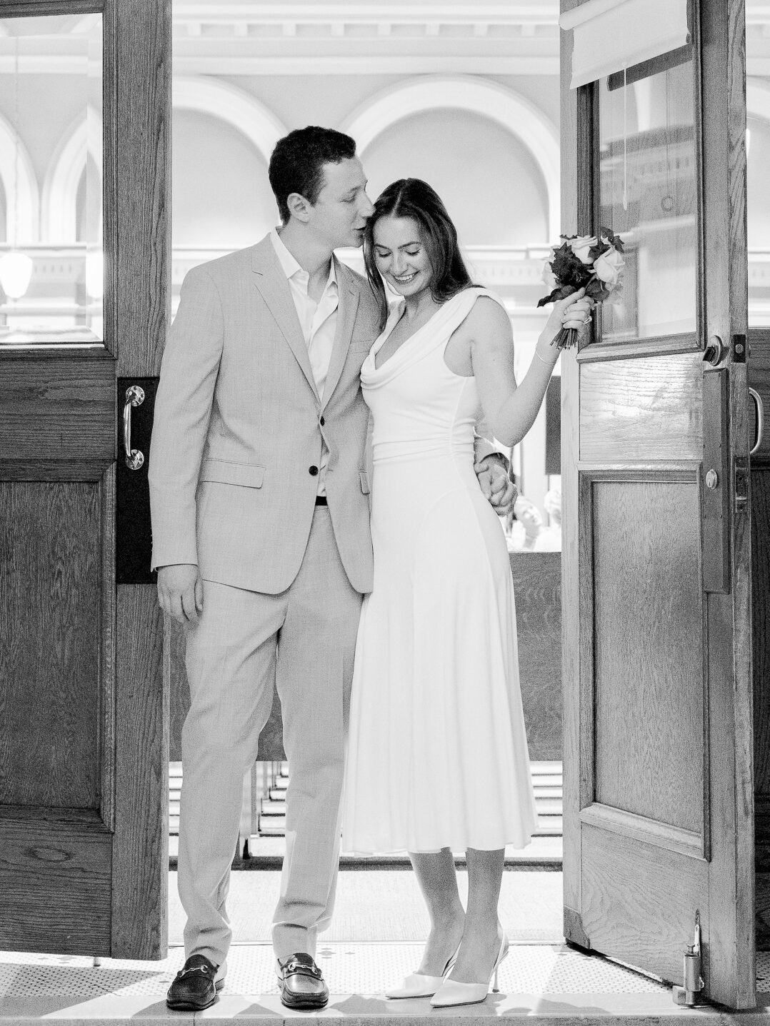 Sweet black and white moment of the bride and groom standing in the courthouse doorway smiling – photographed by Love Tree Studios during their courthouse wedding in Columbia Missouri.