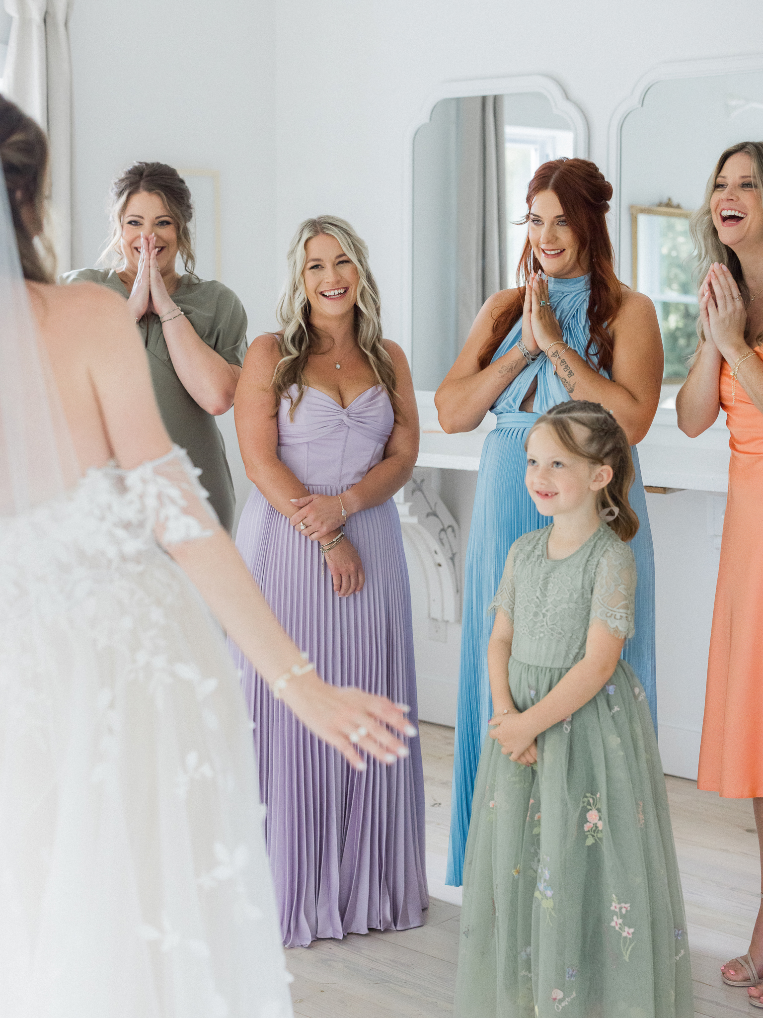 Bridesmaids and flower girl react with smiles and excitement seeing the bride in her gown.