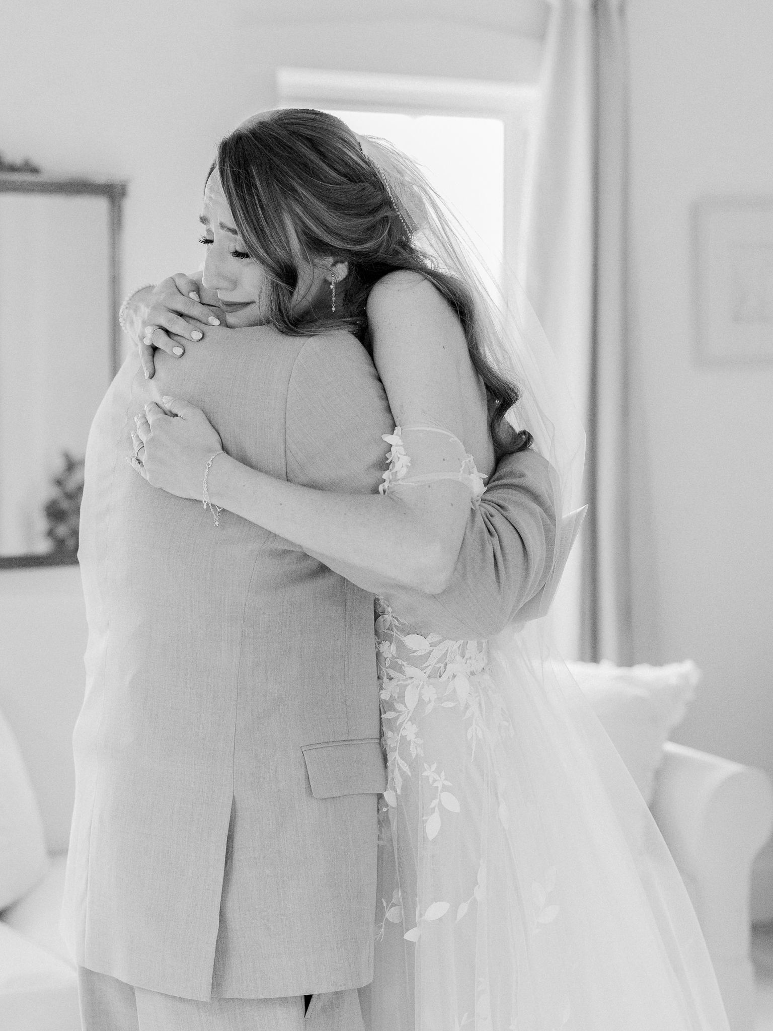 Bride embraces her father in a heartfelt hug, tears in her eyes, during their emotional first look.