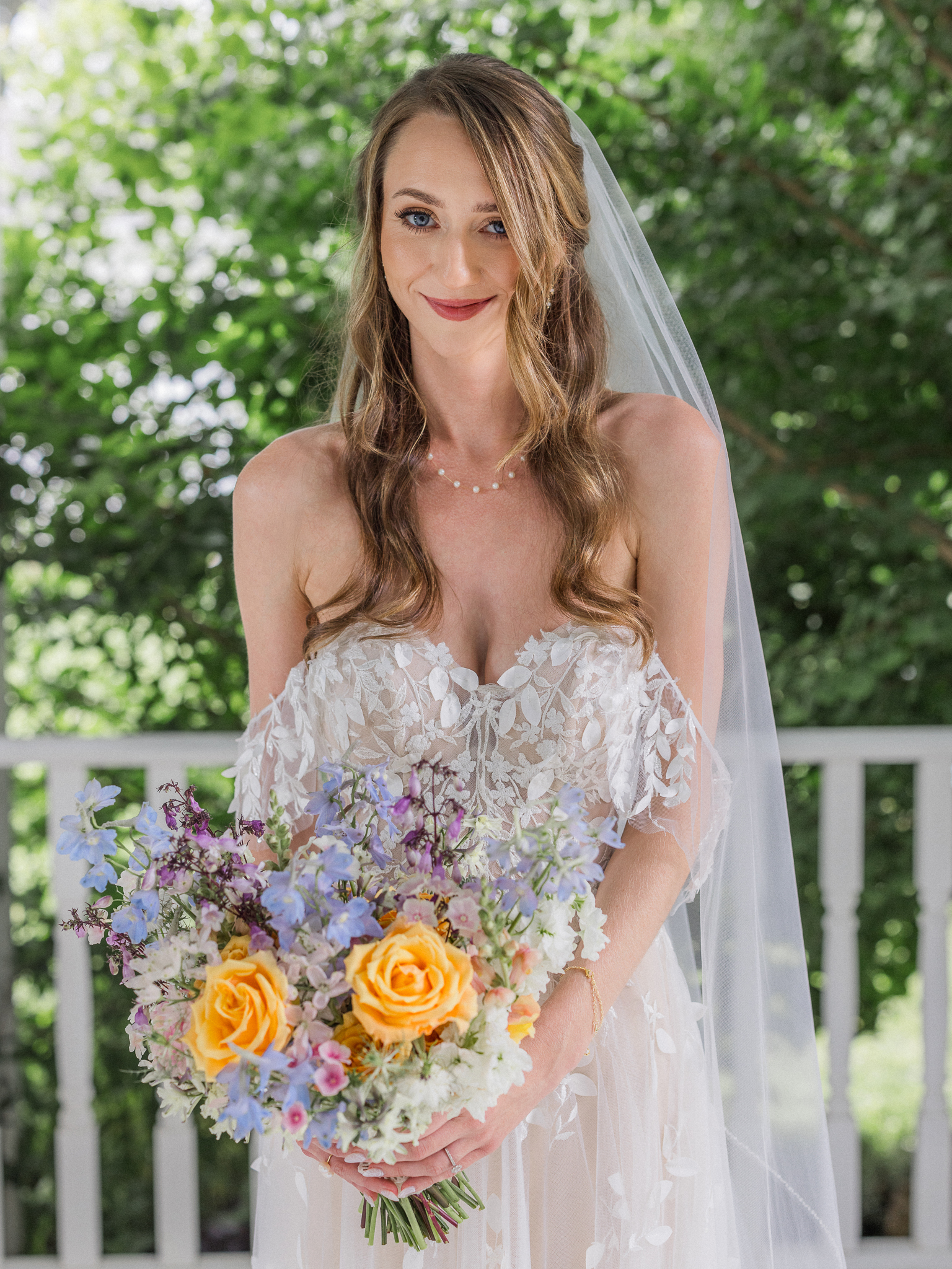 Bride smiling at camera with bouquet in hand and natural greenery in the background at Blue Bell Farm.
