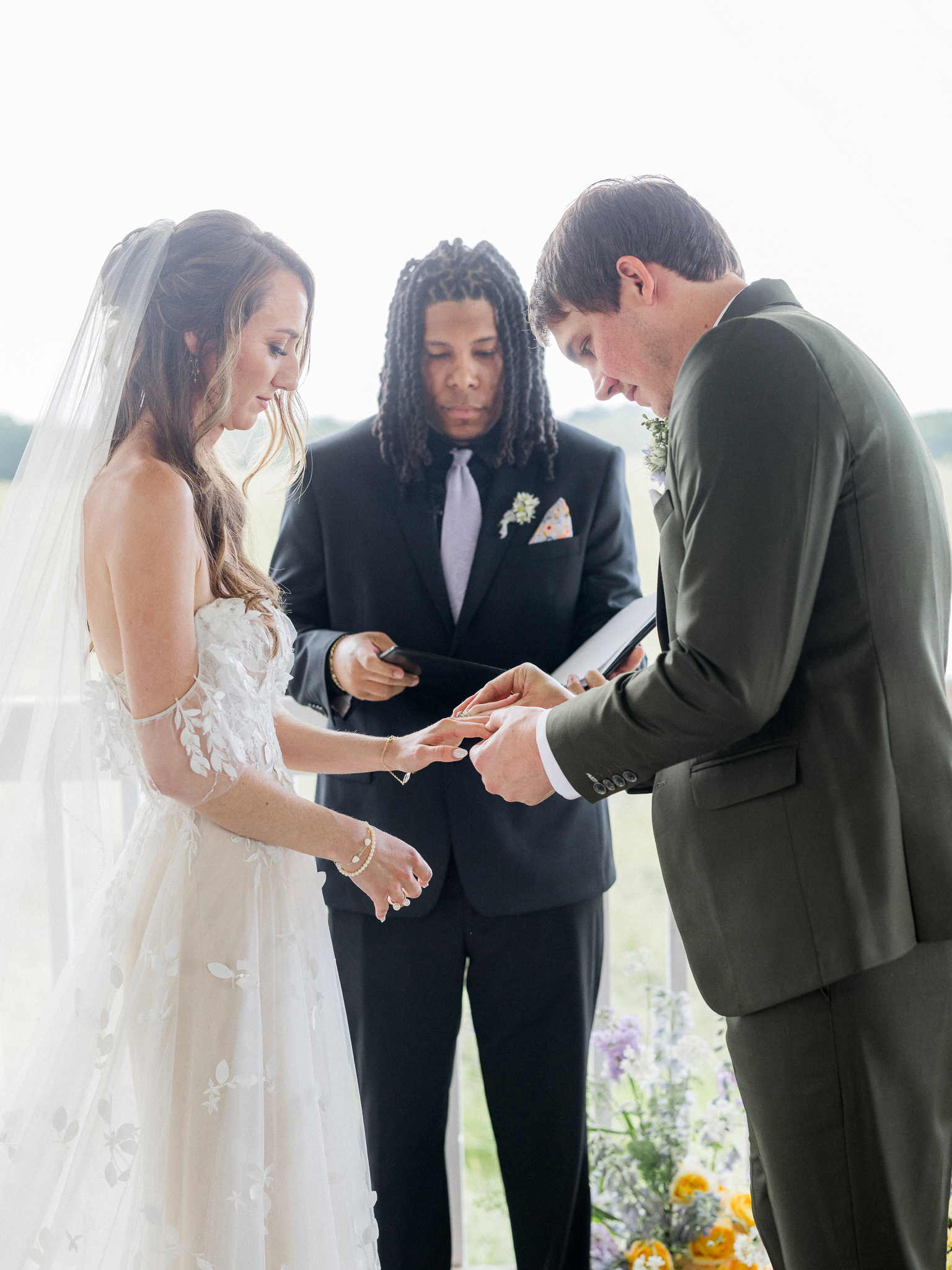 Groom places ring on bride’s finger as the officiant looks on during a Blue Bell Farm wedding ceremony.