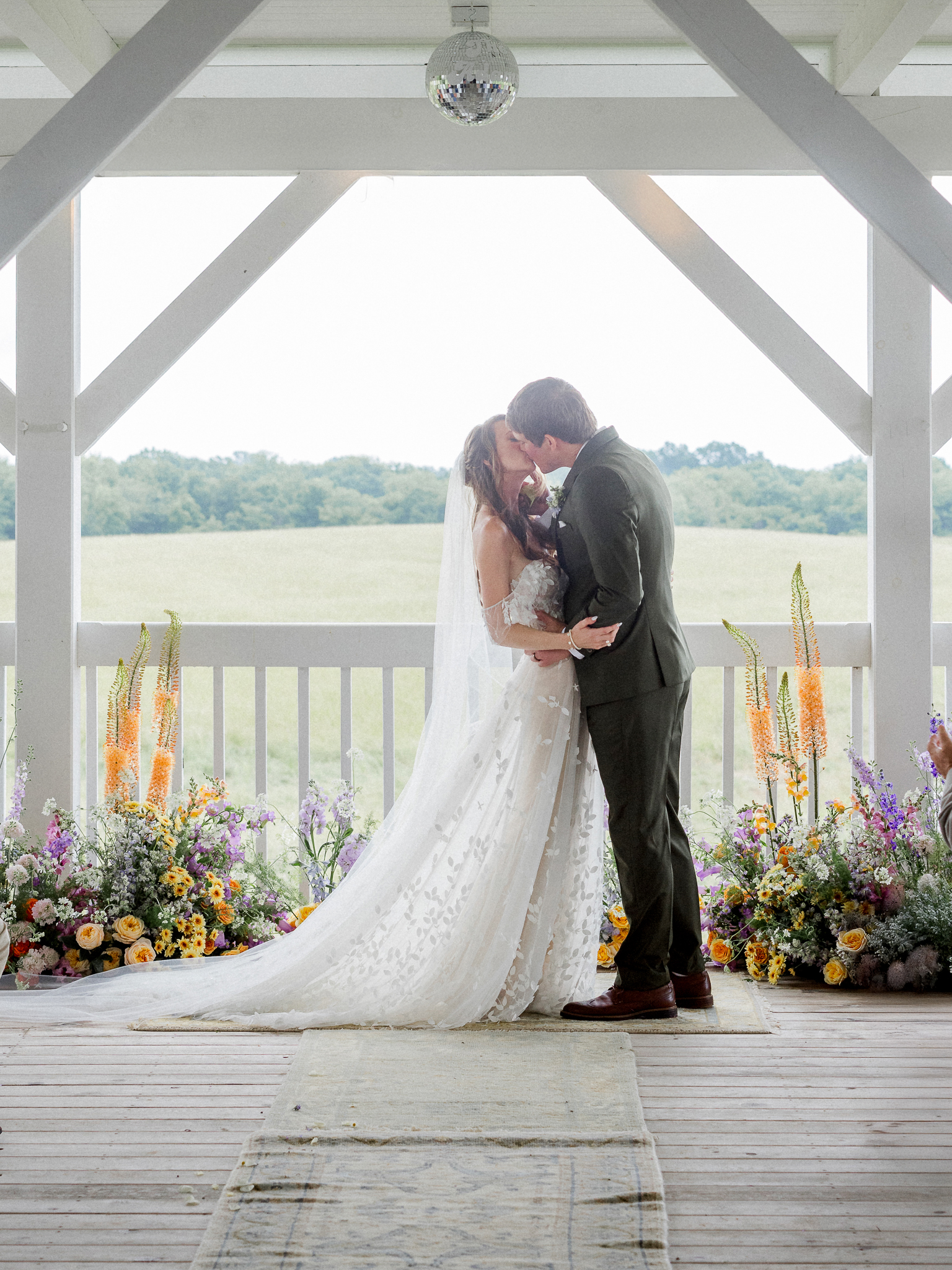 Bride and groom share their first kiss as newlyweds under a flower-filled altar at a Blue Bell Farm wedding.