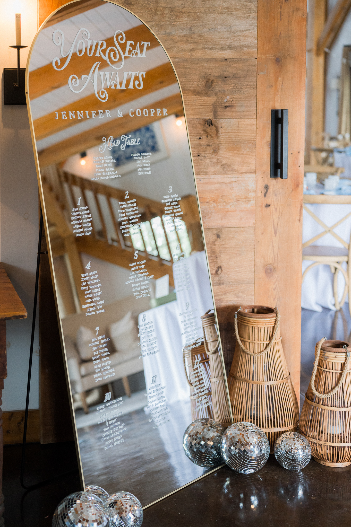 Mirrored seating chart with the words “Your Seat Awaits” and guest names, surrounded by lanterns and disco balls.
