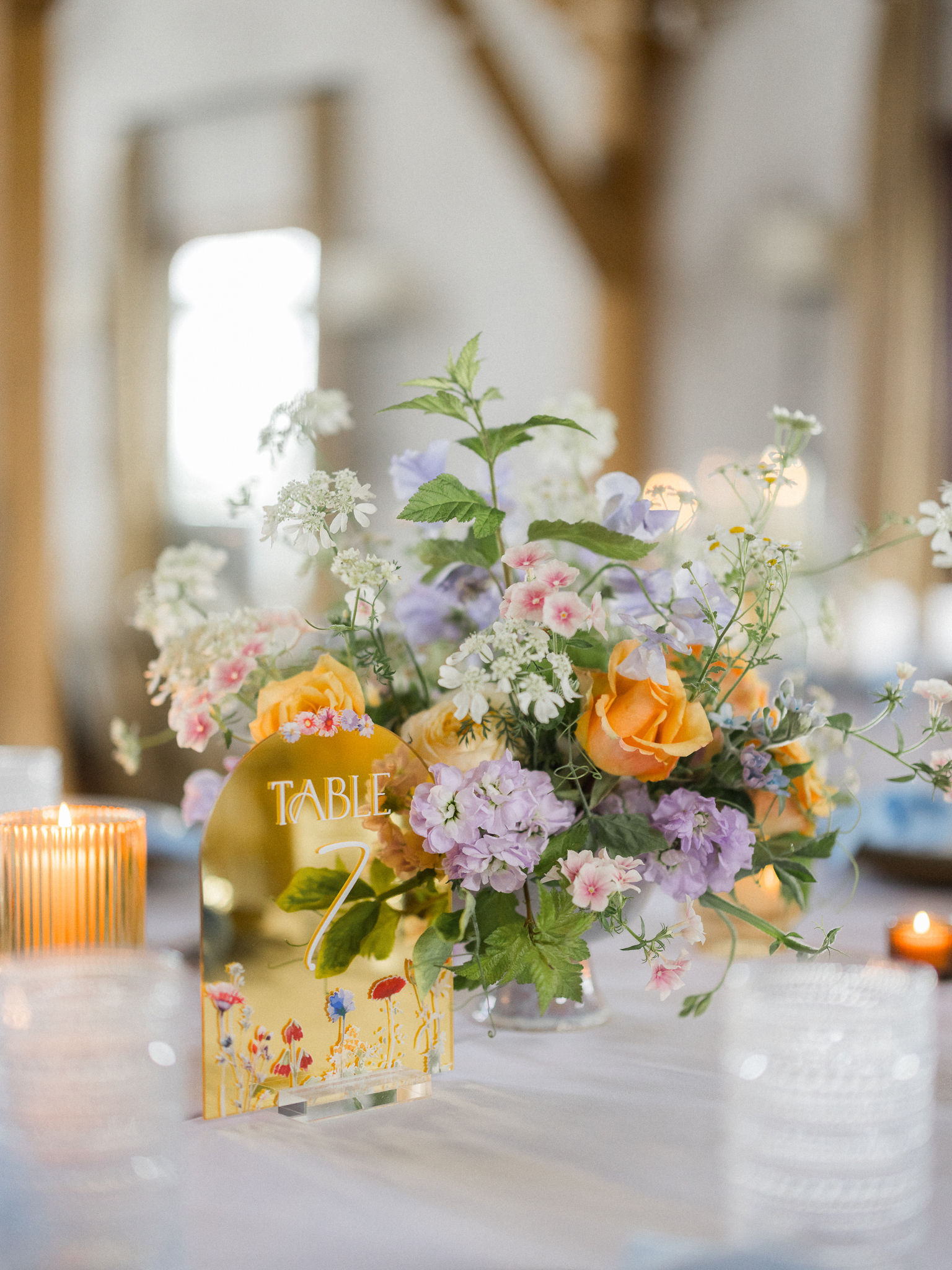 A colorful wildflower centerpiece with a mirrored “Table 7” sign on a beautifully decorated reception table.