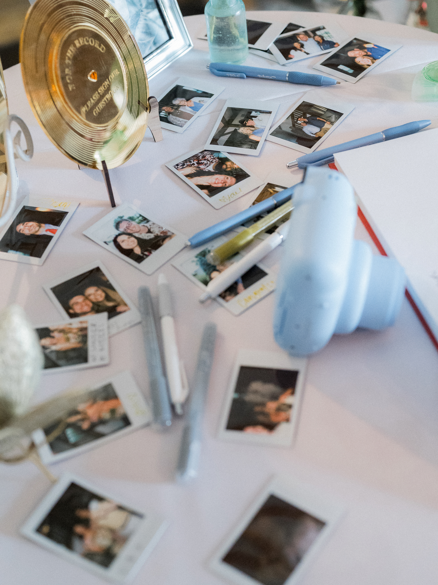 Table filled with instant photos, pens, and a mini camera as part of the wedding guestbook setup.