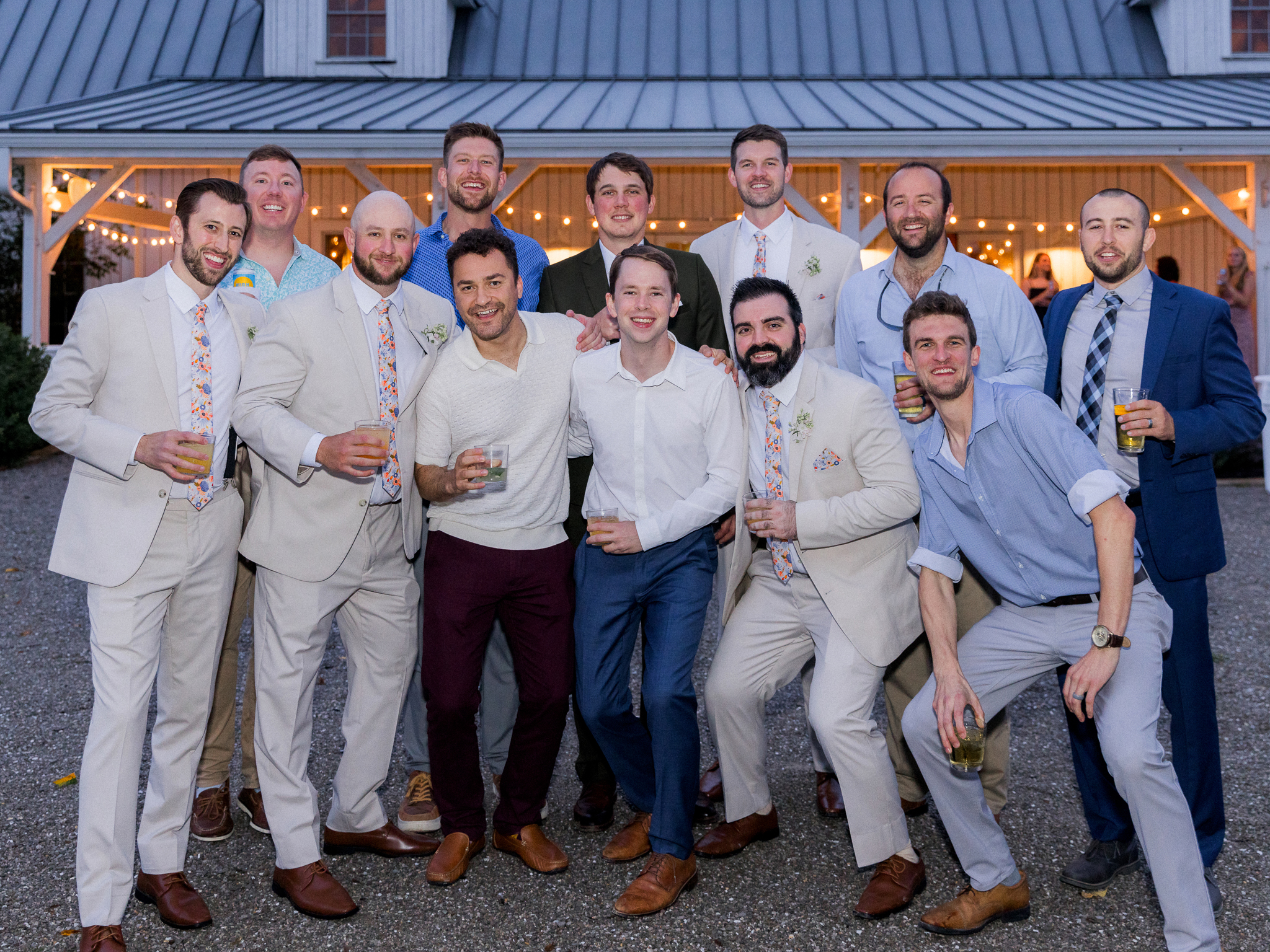 The groom poses with a large group of his groomsmen and friends outside the reception barn at Blue Bell Farm, captured by Love Tree Studios.