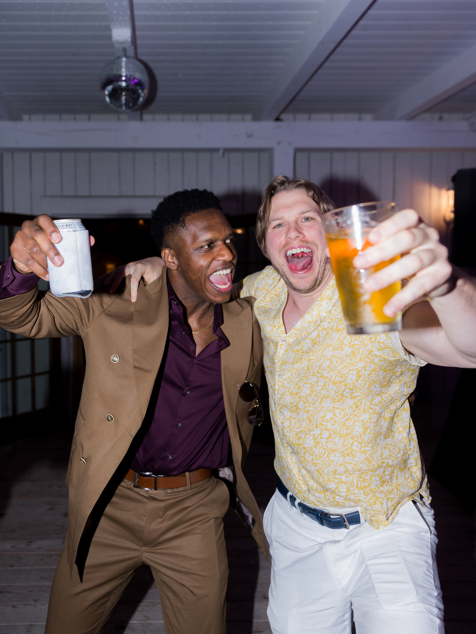 Two wedding guests cheer with drinks in hand, dancing under the lights at a Blue Bell Farm wedding reception captured by Love Tree Studios.