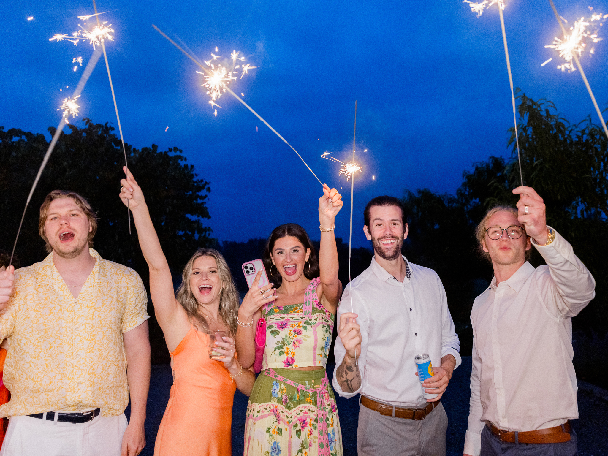 Guests smile and hold sparklers in a joyful nighttime celebration during a Blue Bell Farm wedding, beautifully captured by Love Tree Studios.