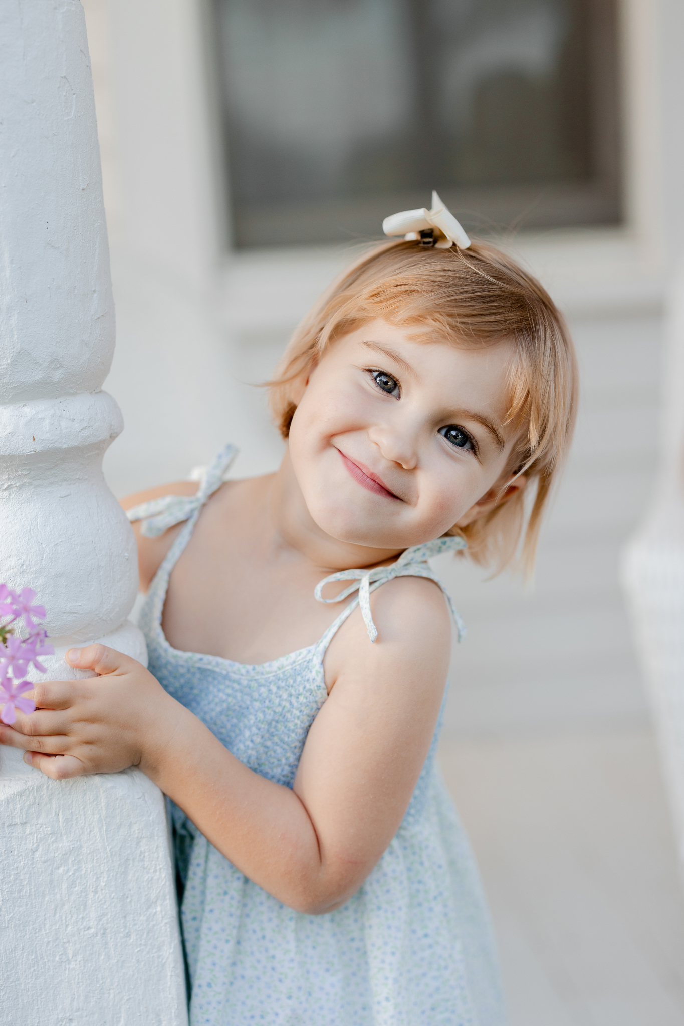 Young girl in blue dress smiling on farmhouse porch during Missouri family photography session