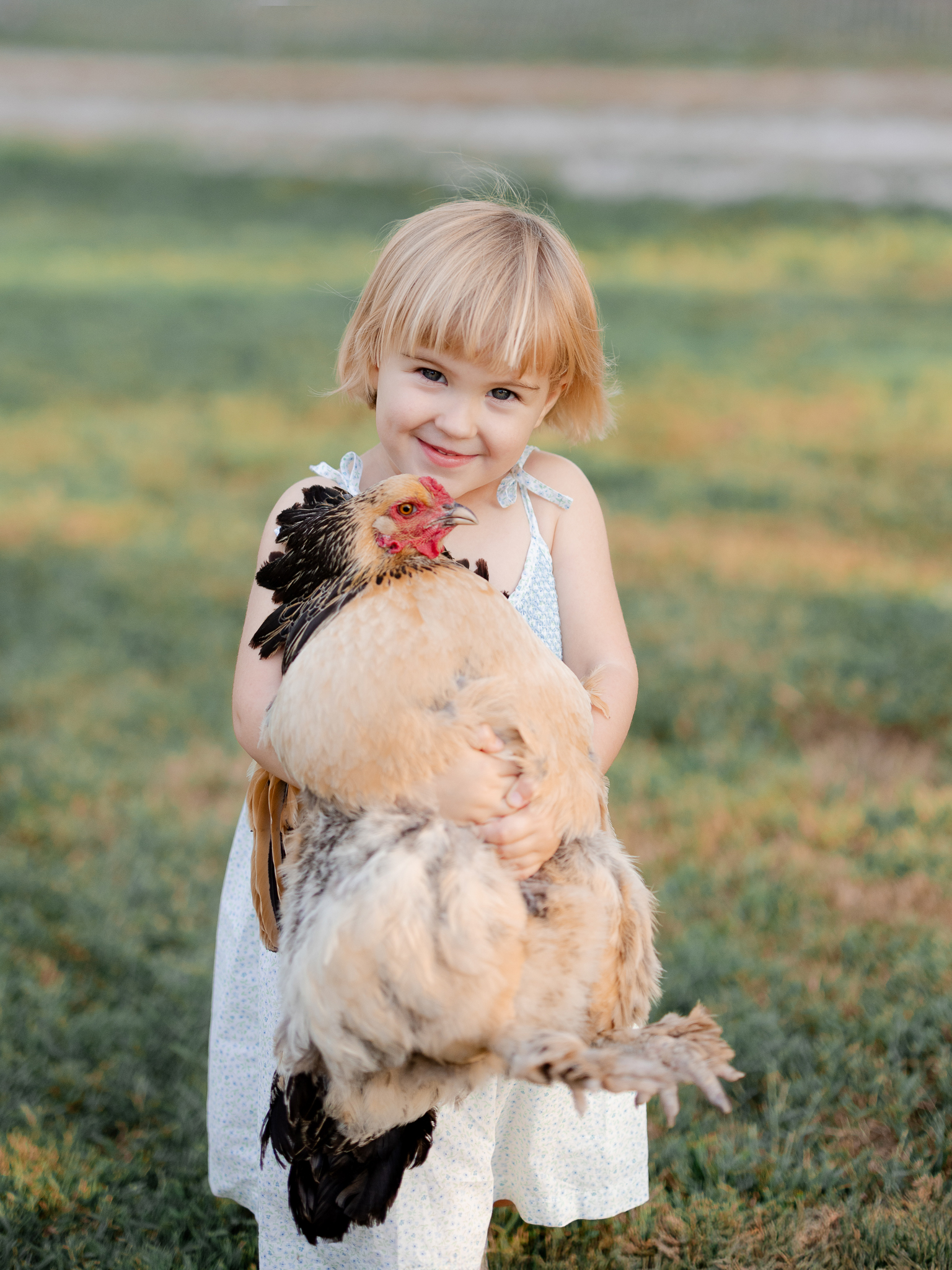 Young daughter holding a chicken while smiling — Love Tree Studios, Missouri family photographer.