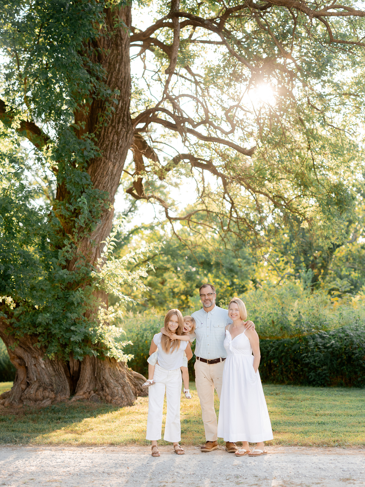 Family of four standing together under tall trees — Love Tree Studios, Missouri family photographer.