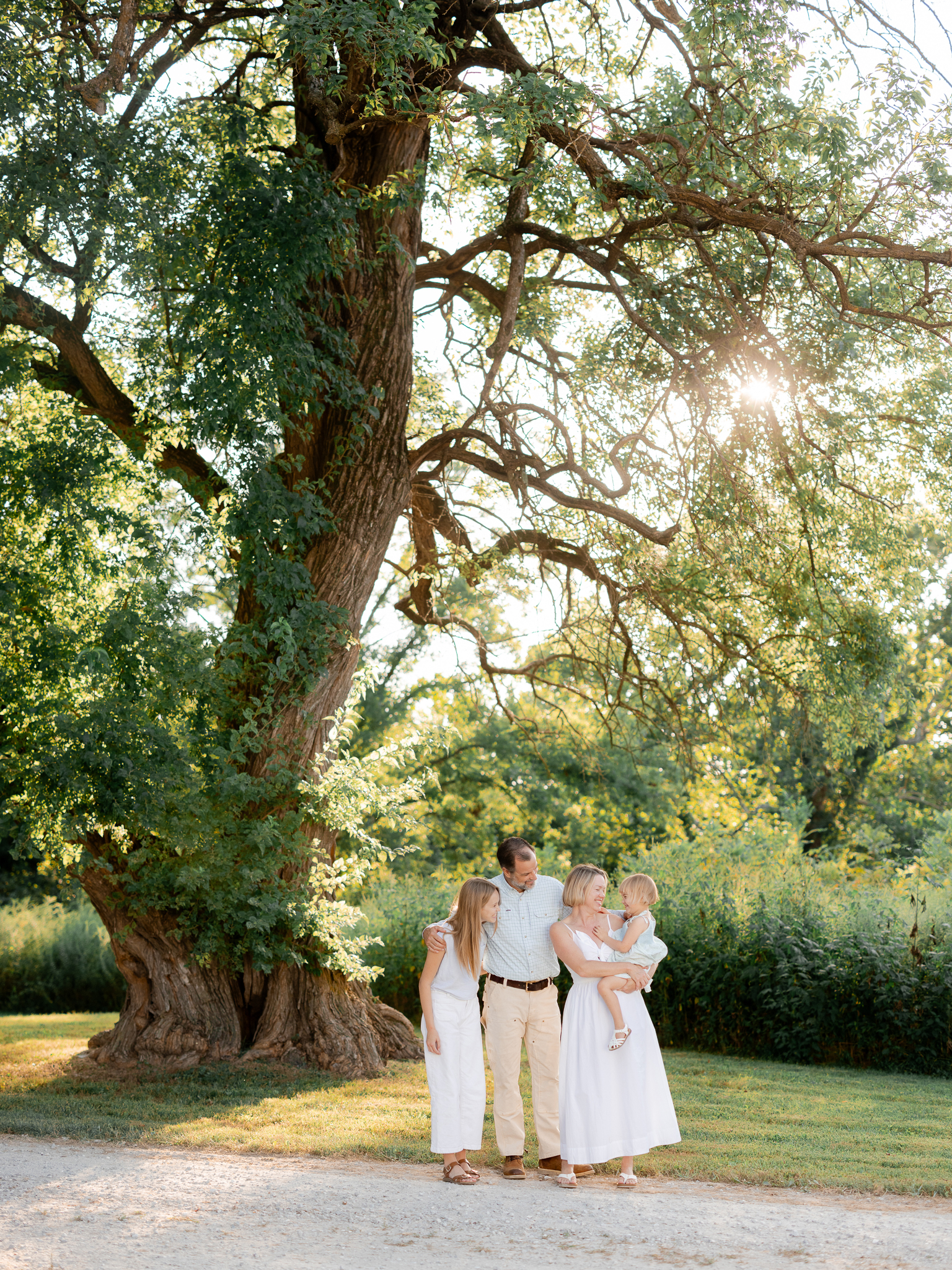 Family standing together and laughing under tall trees at Blue Bell Farm — Love Tree Studios, Missouri family photographer.