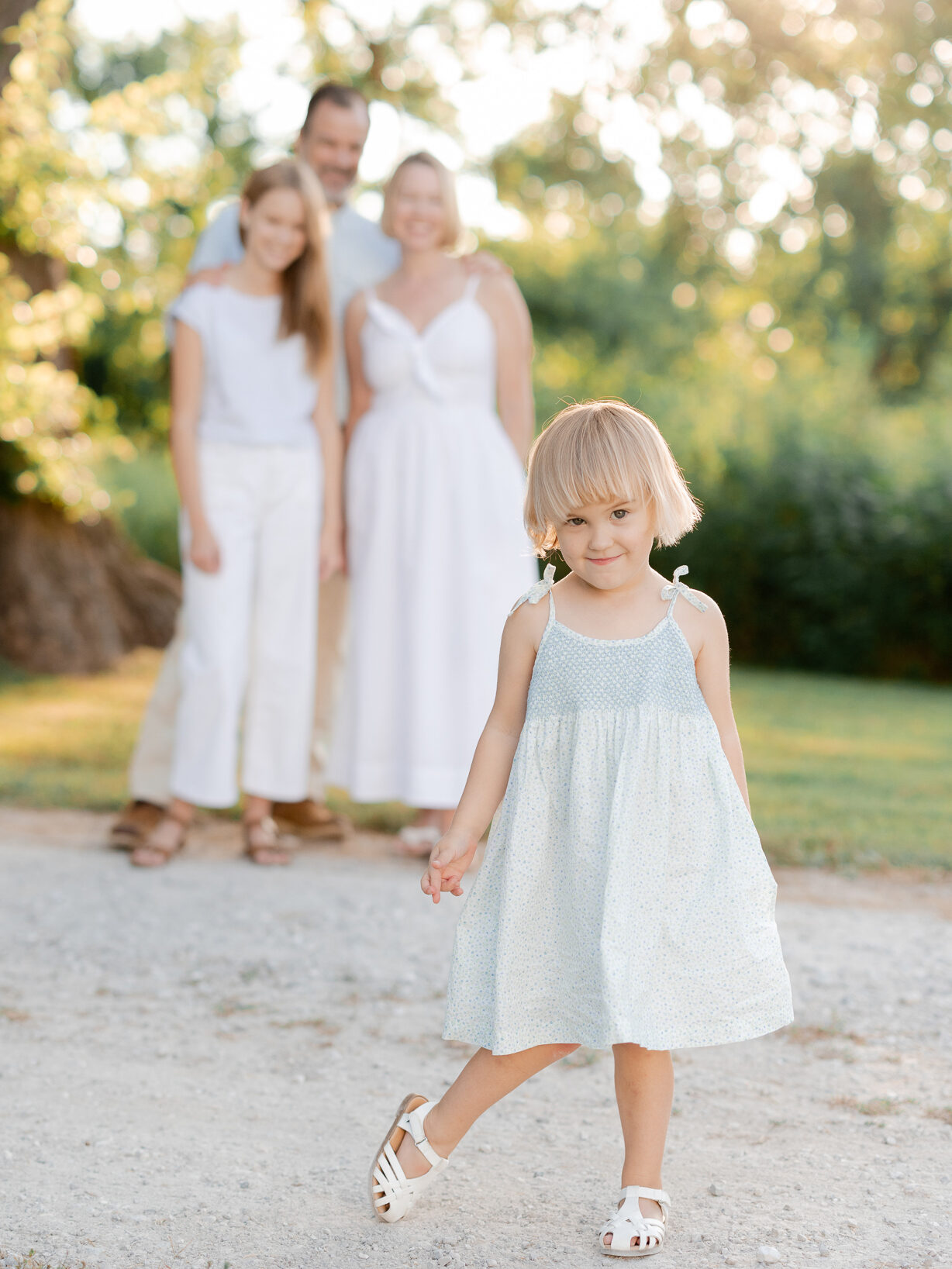 Toddler walking ahead with family blurred in the background — Love Tree Studios portraits.