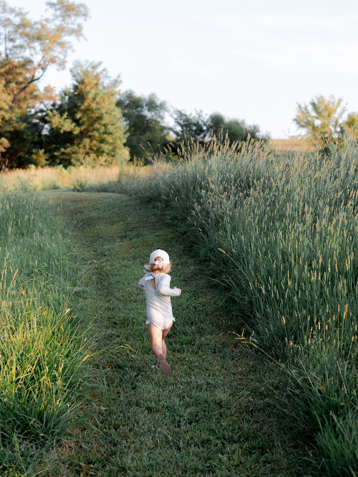 Child running down grassy path in summer fields — captured by Missouri family photographer.