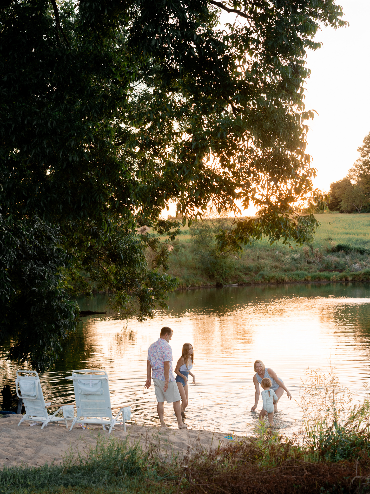 Family walking along sandy lake beach during golden hour — Missouri family photographer.