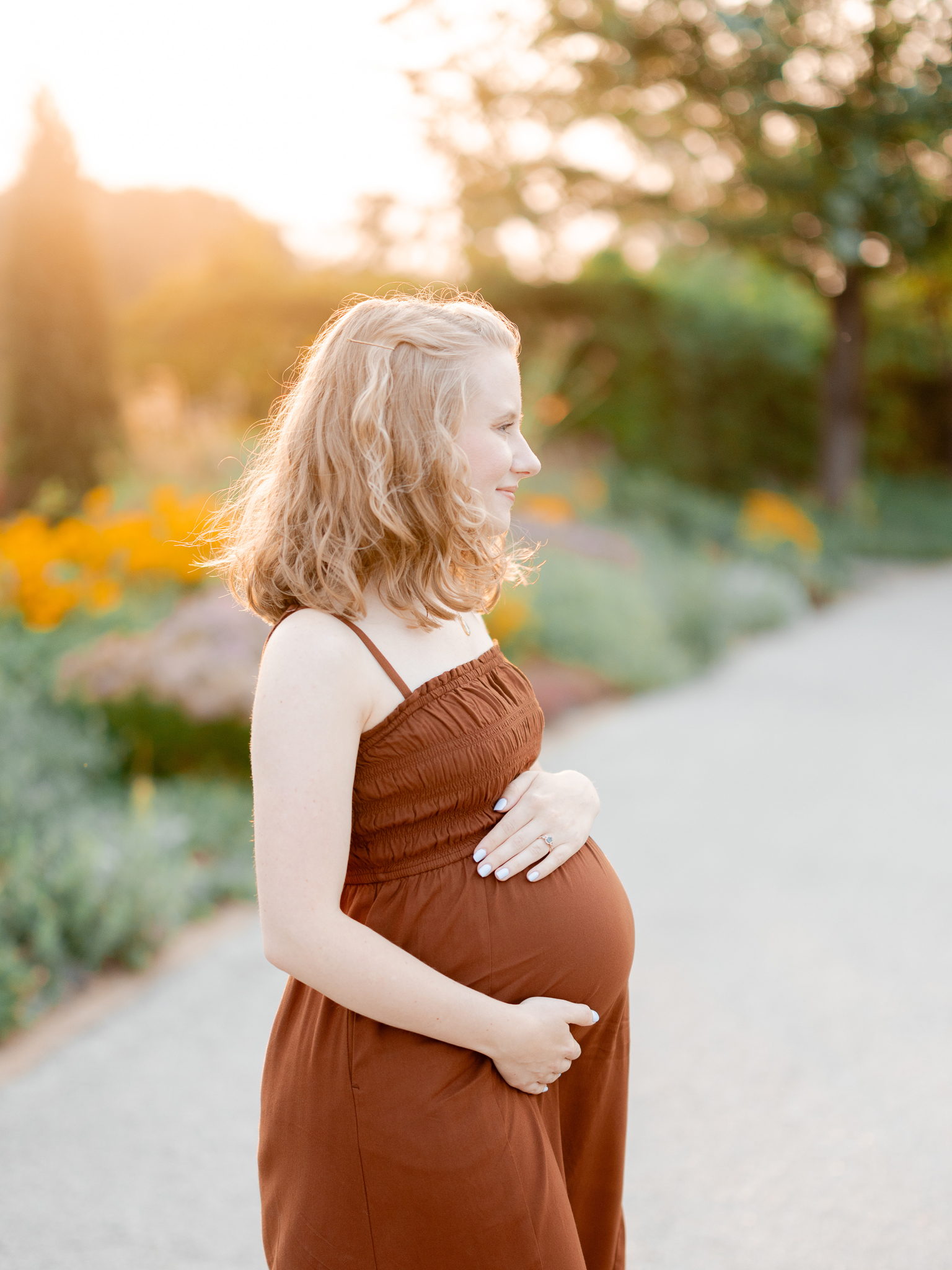 Mother-to-be cradling her belly in golden light with wildflowers in the background at Art Hill, St. Louis maternity session by Love Tree Studios.