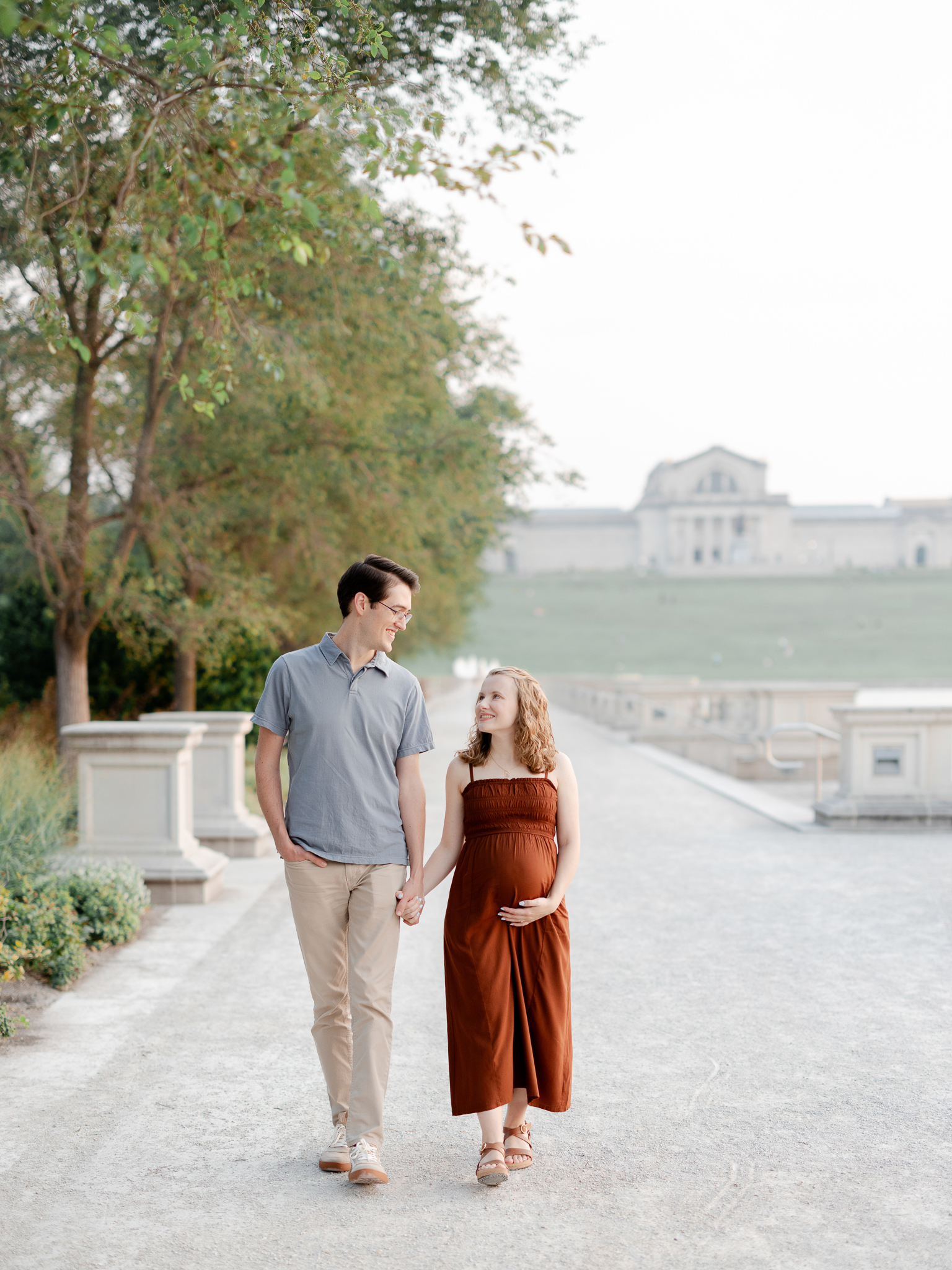 Parents-to-be walk together smiling during their Art Hill maternity session in St. Louis, captured by Love Tree Studios photographer.