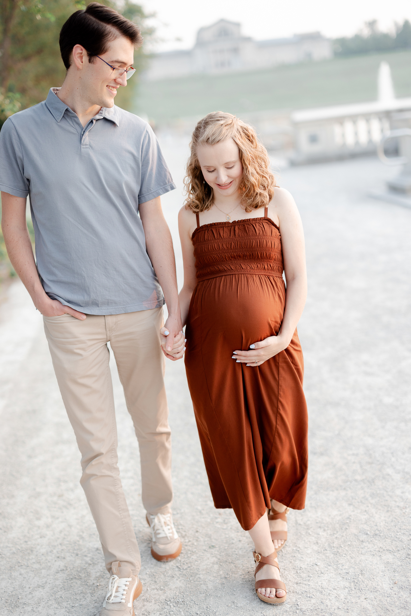Maternity portraits of a couple walking hand in hand near the fountains of Art Hill in St. Louis, captured by Love Tree Studios.