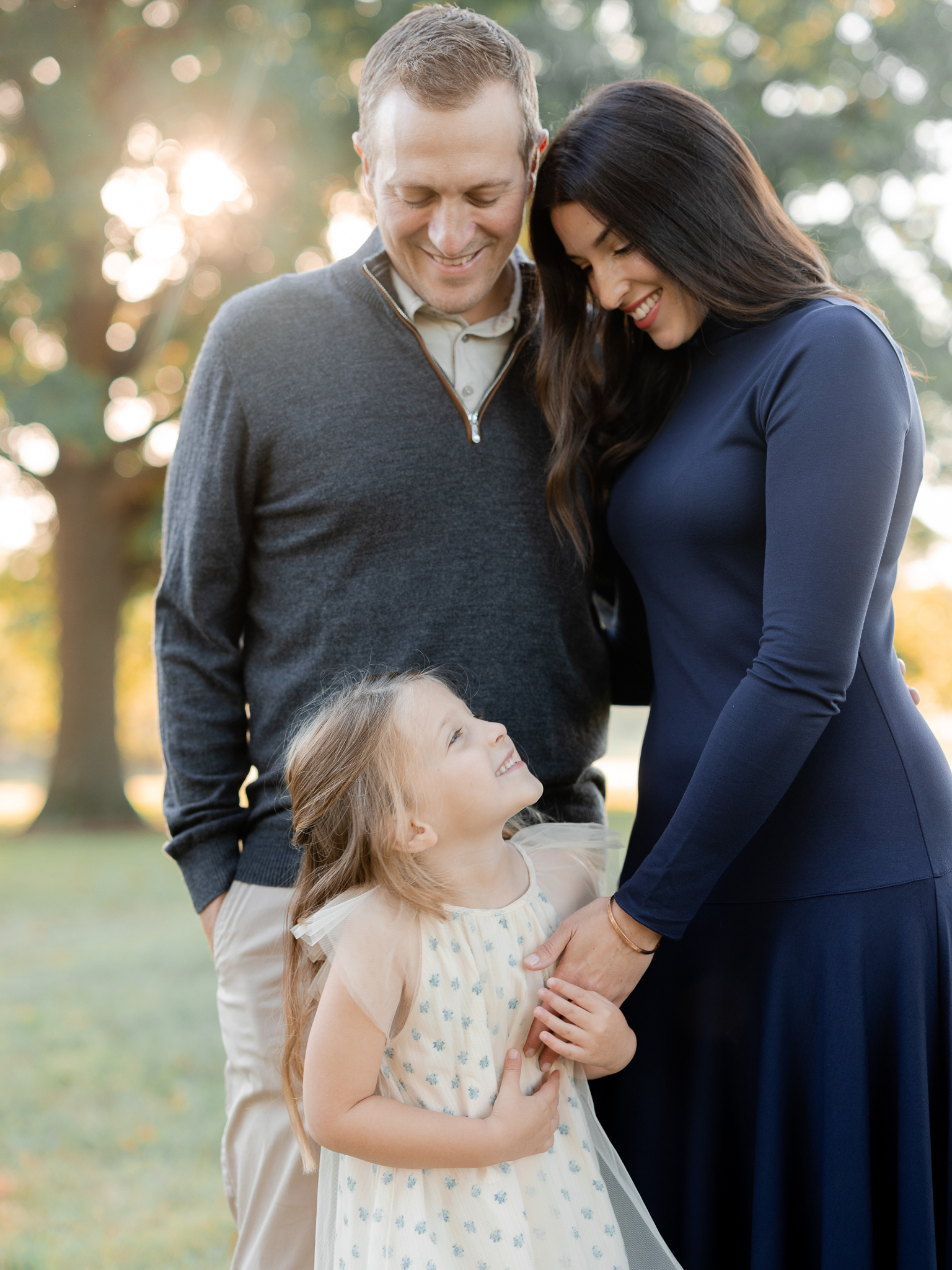 Parents smiling down as daughter looks up lovingly during sunrise family photos in Columbia Missouri.