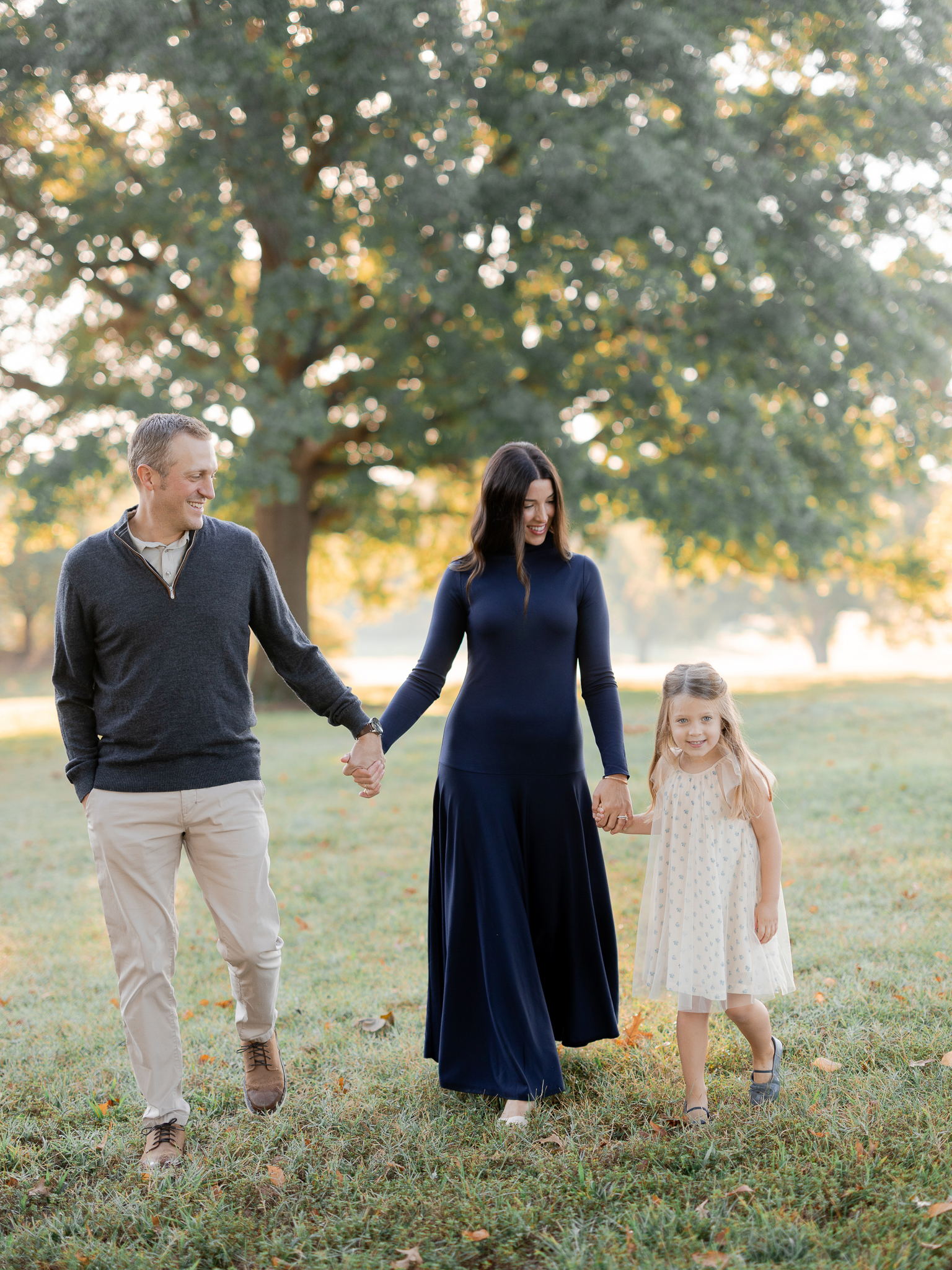 Family walking hand in hand across dewy grass during sunrise family photos Columbia Missouri.
