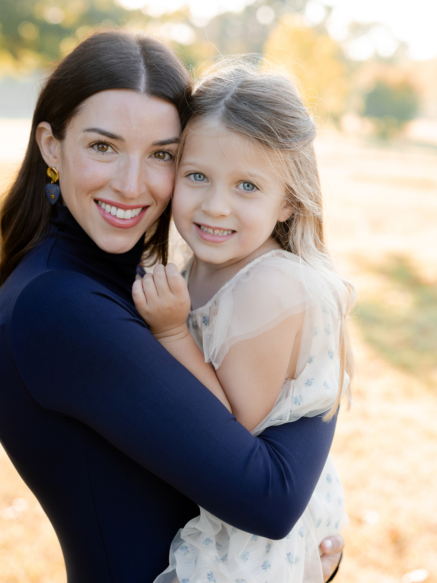 Mother holding daughter cheek-to-cheek with fall colors glowing – Columbia Missouri sunrise family portraits.