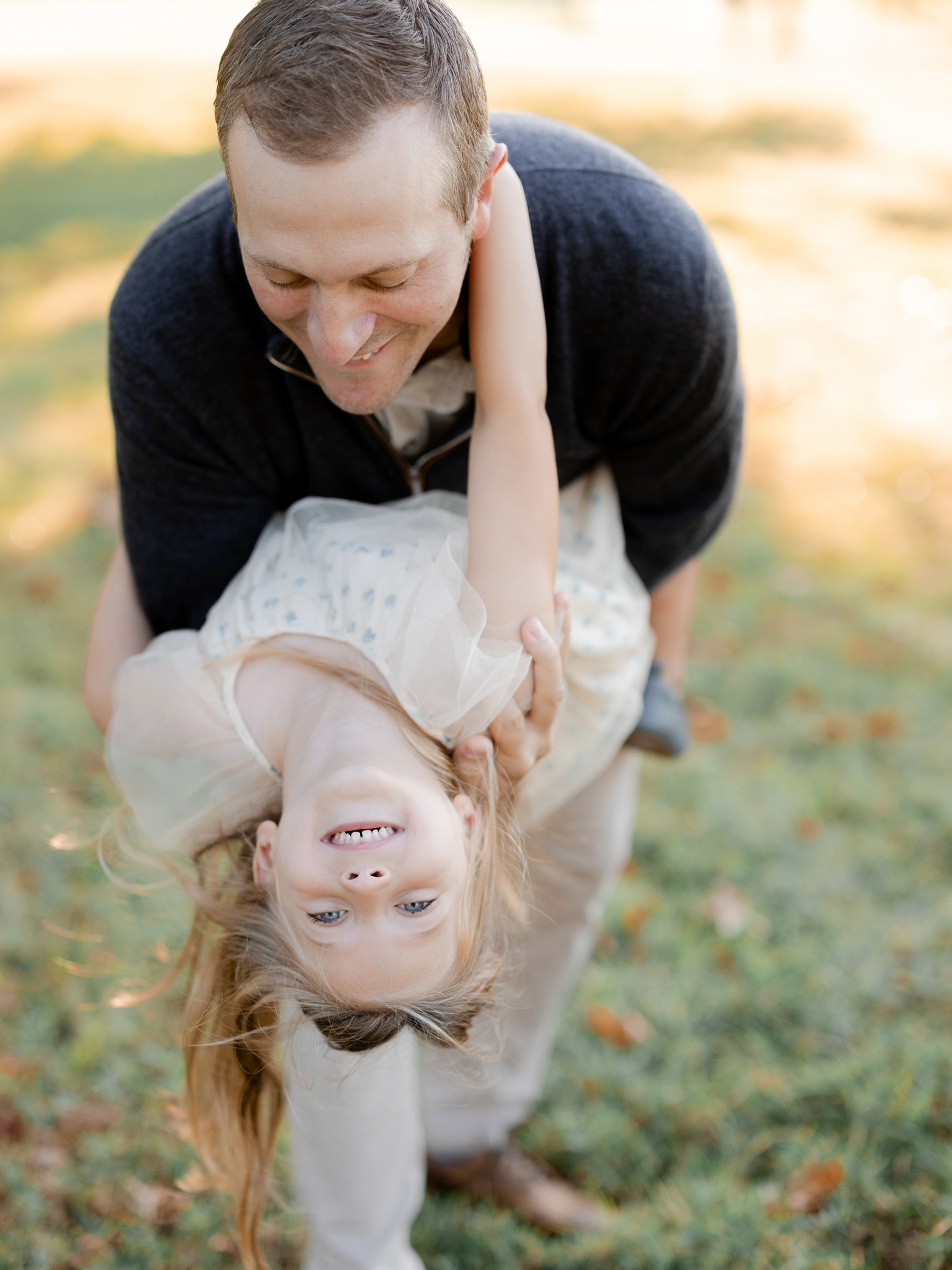 Daughter giggling upside down as her dad playfully swings her during sunrise family photos Columbia Missouri.