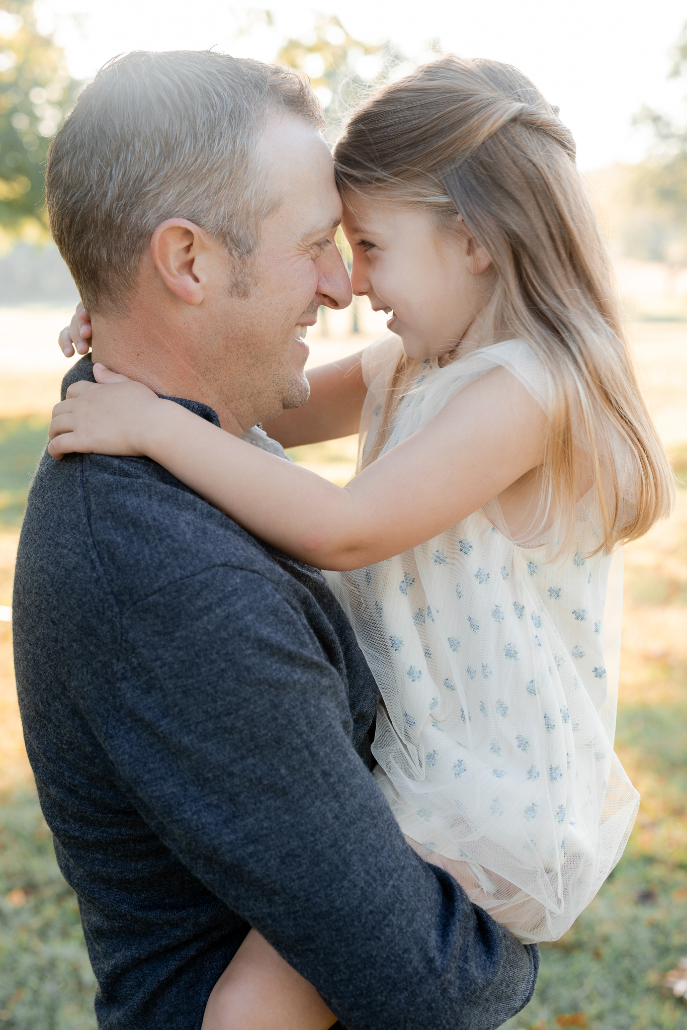 Family sitting together under a large oak tree, cuddling in the morning glow – sunrise family session Columbia Missouri.