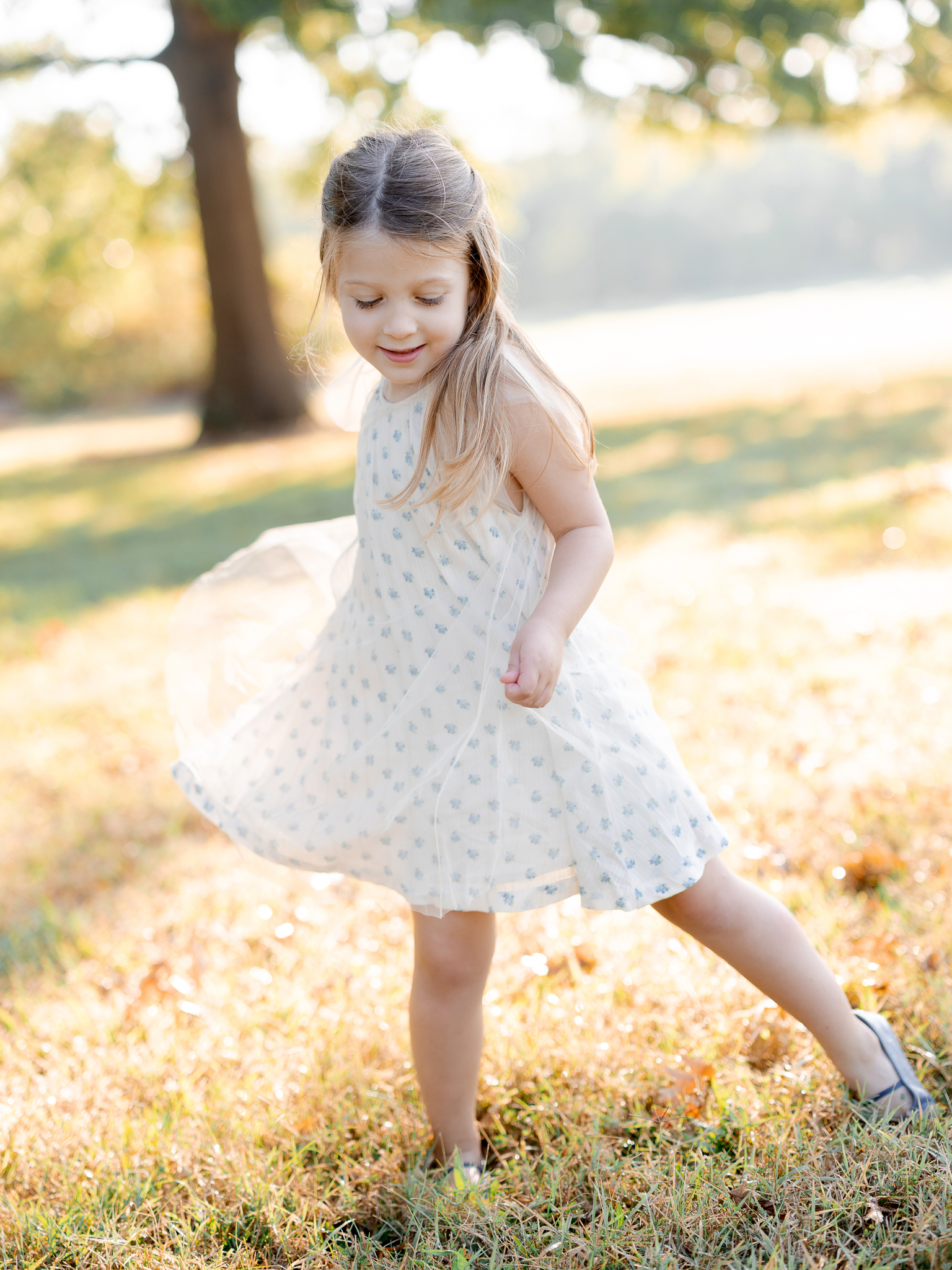 Little girl twirling in a light dress with sunshine on her hair – Columbia Missouri sunrise family photography.