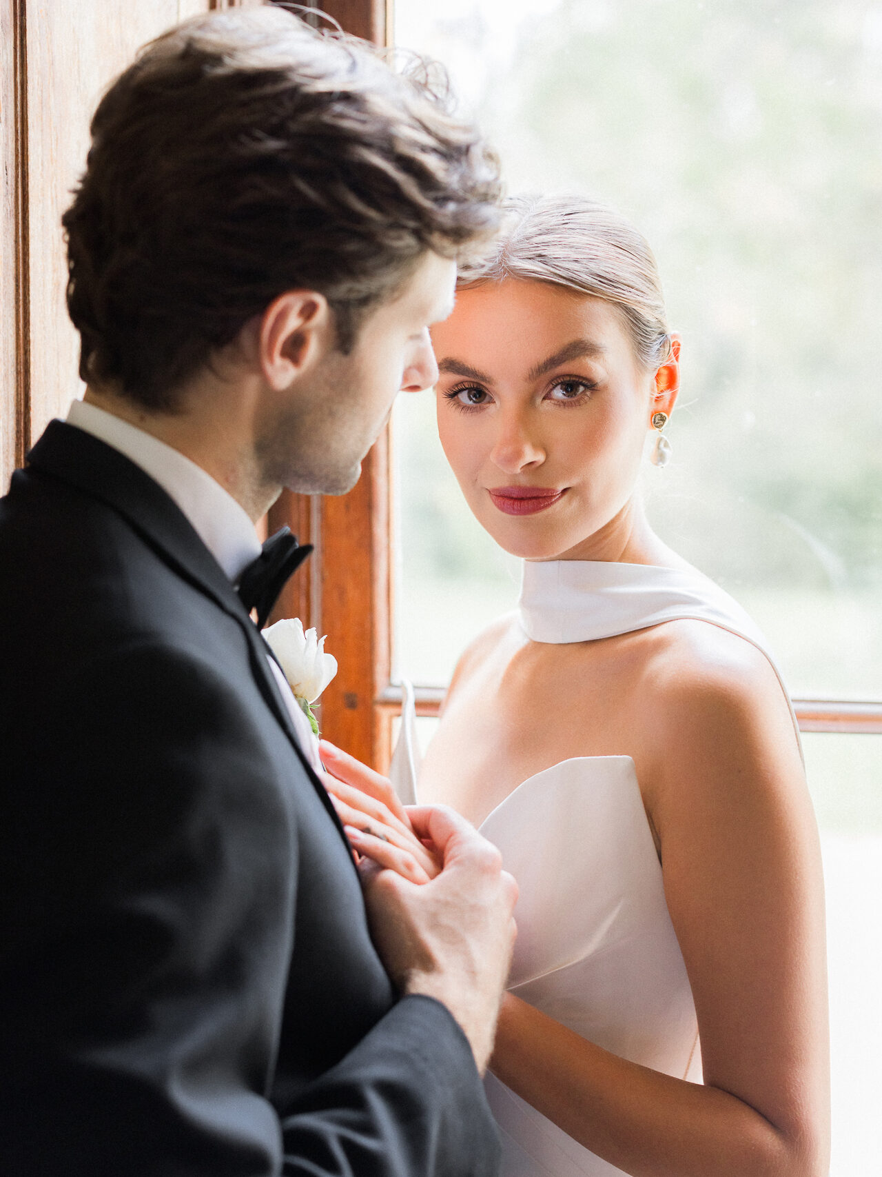 Bride in a modern white gown gazing softly at the camera while holding hands with her groom during a Château de Thauvenay wedding in France.