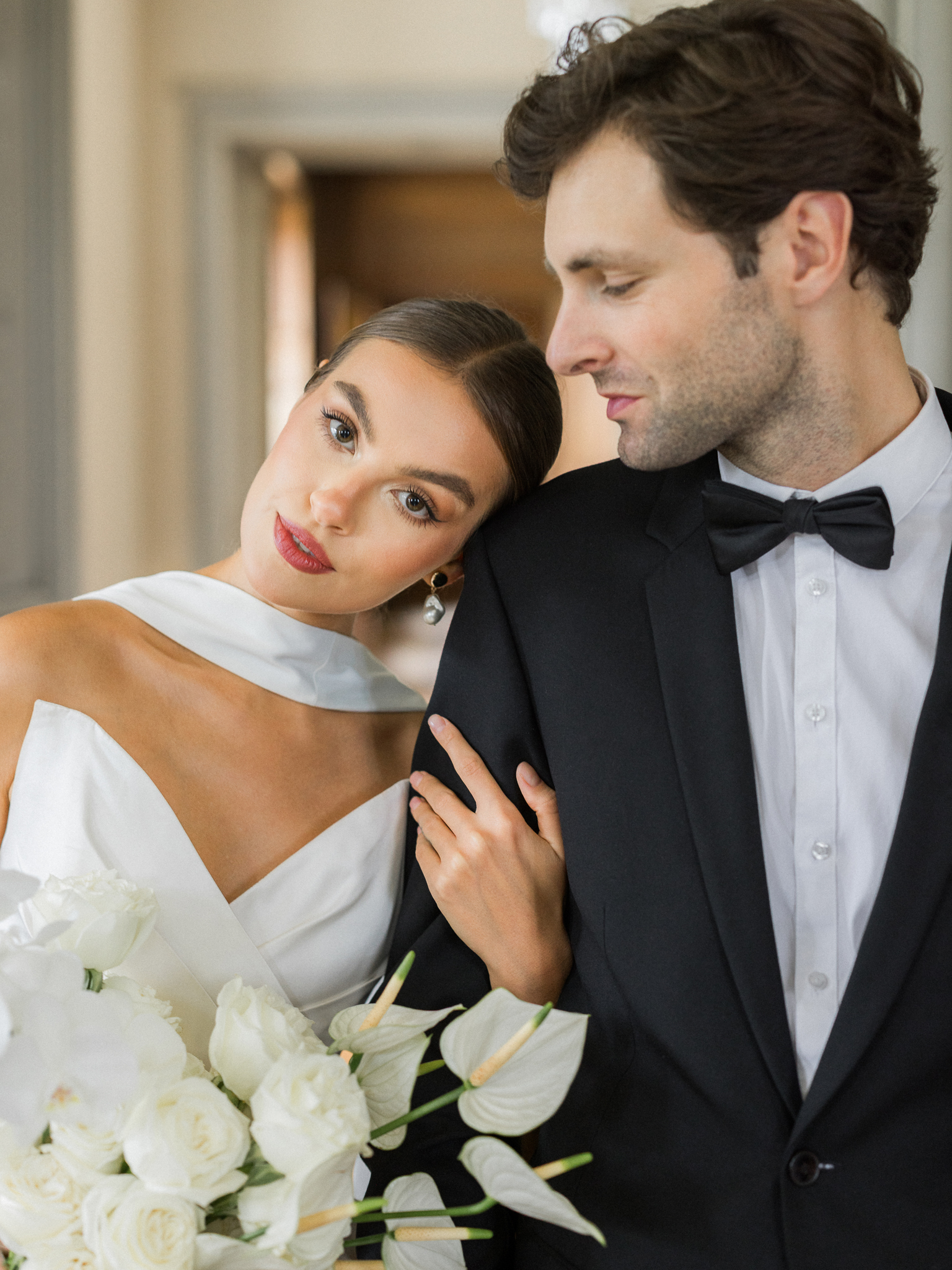 Bride leaning on groom’s shoulder with a bouquet of white roses and anthuriums during a timeless Château de Thauvenay wedding editorial.