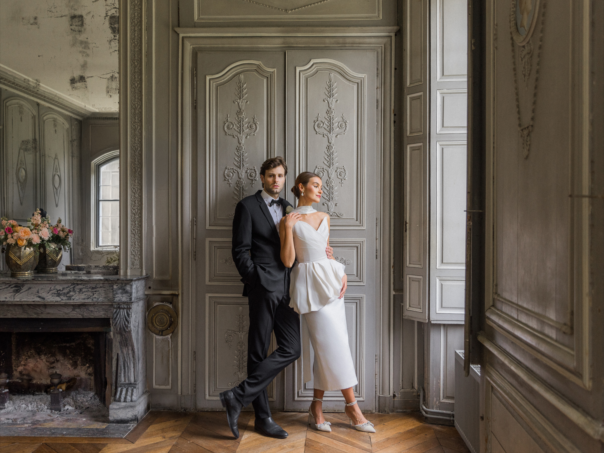 Bride and groom embracing in front of detailed gray paneling and a marble fireplace at Château de Thauvenay, photographed by Love Tree Studios.