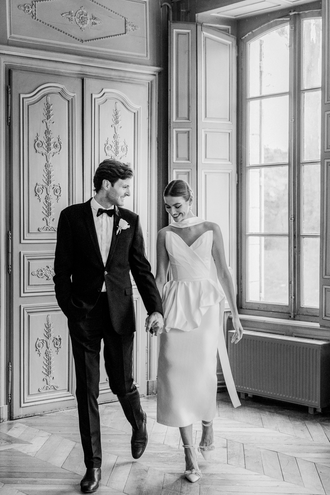 Black and white image of bride resting her head on groom’s shoulder beneath ornate French molding at Château de Thauvenay, photographed by Love Tree Studios.