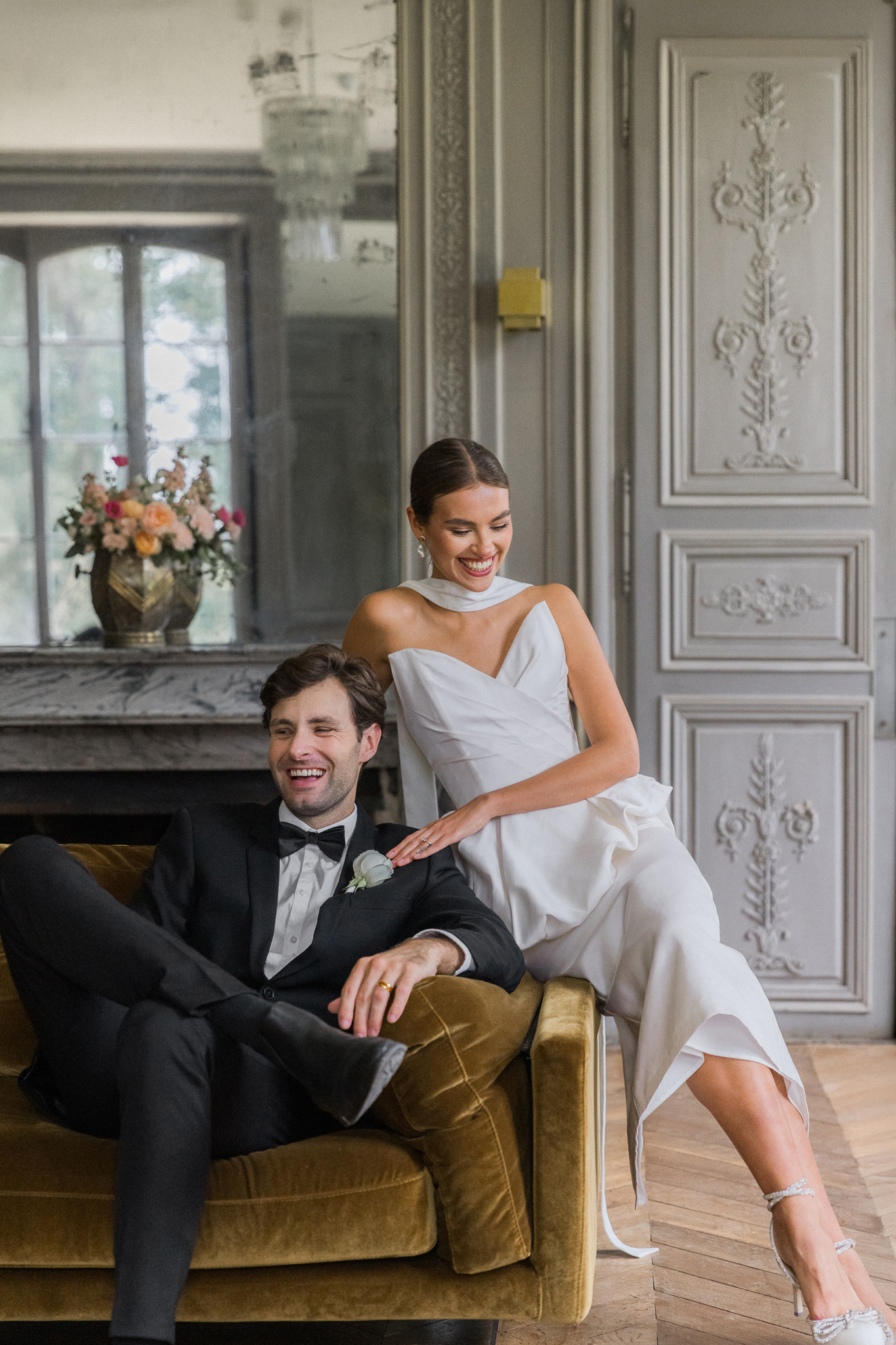 Bride and groom sharing a joyful laugh on a vintage velvet sofa during their Château de Thauvenay wedding editorial, photographed by Love Tree Studios.