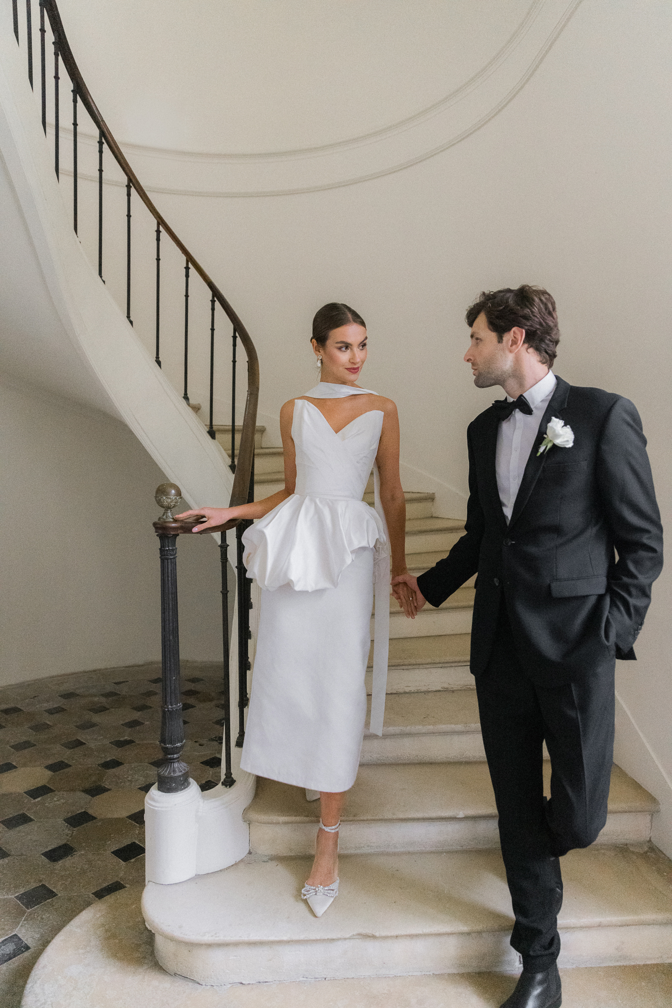 Bride and groom holding hands on a sweeping staircase inside Château de Thauvenay during their fine art destination wedding in France, captured by Love Tree Studios.