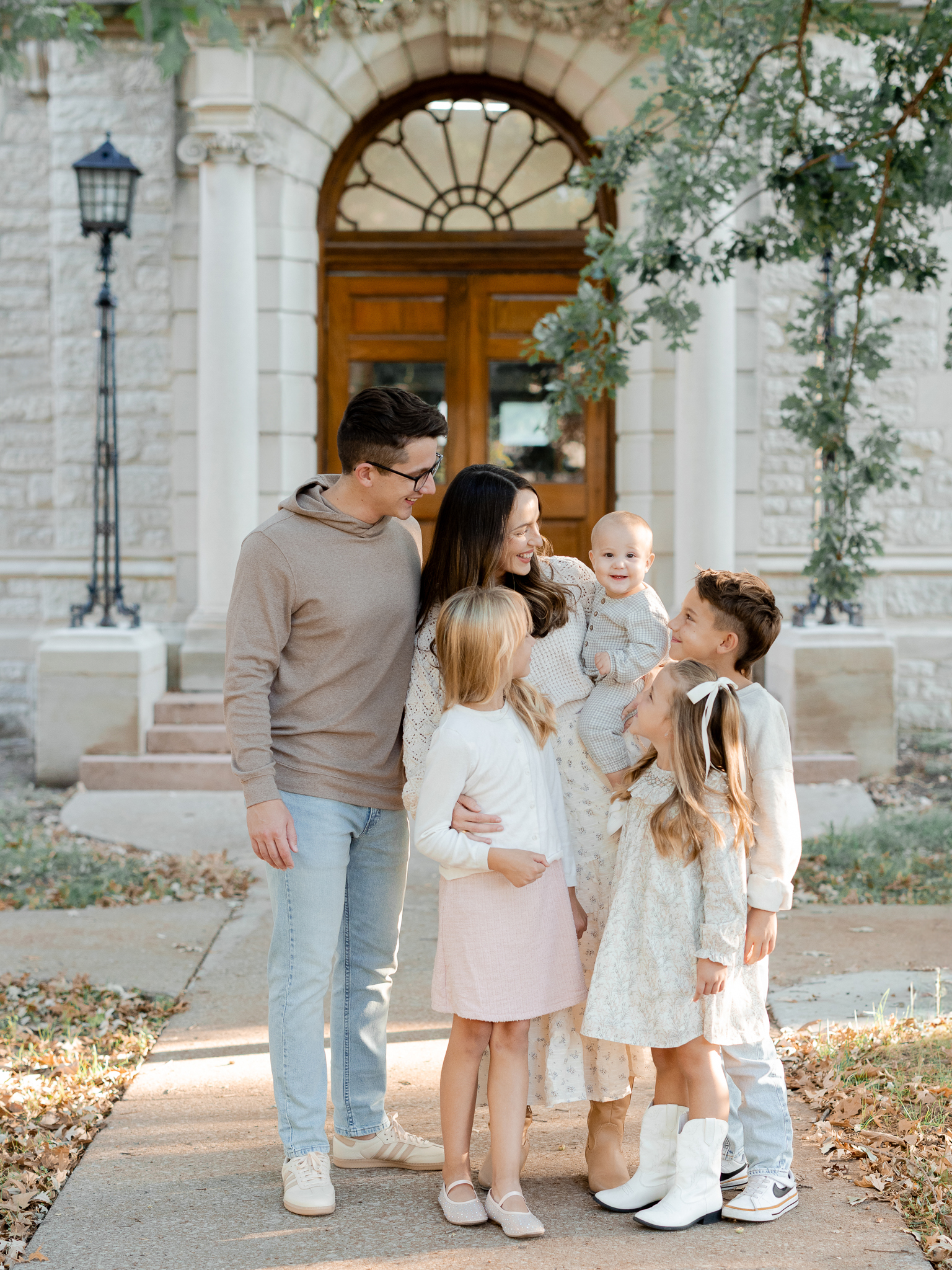 Parents and children smiling and looking at each other in front of a historic Columbia building, by Columbia Missouri family photographer.