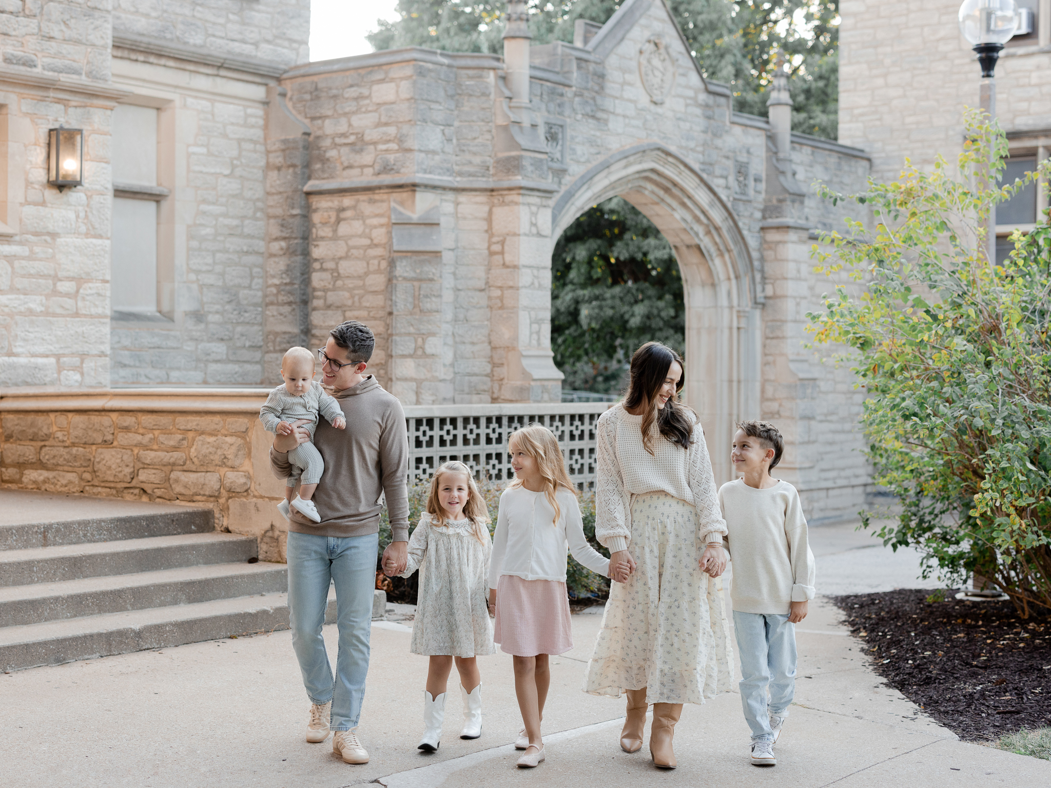 The Bedford family holding hands and walking near historic stone arches during a golden-hour session, Columbia Missouri family photographer.