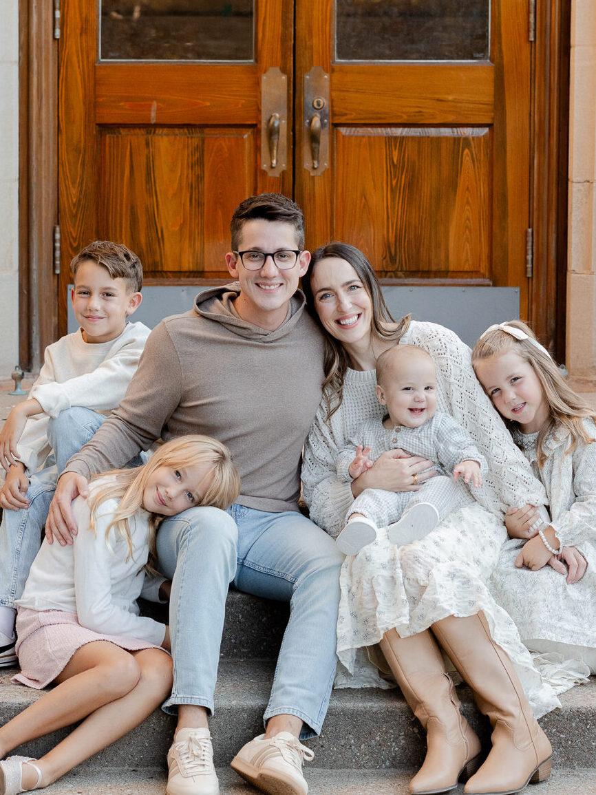 Parents with their four children sitting closely together on steps of a Columbia landmark, photographed by Love Tree Studios, Columbia Missouri family photographer.