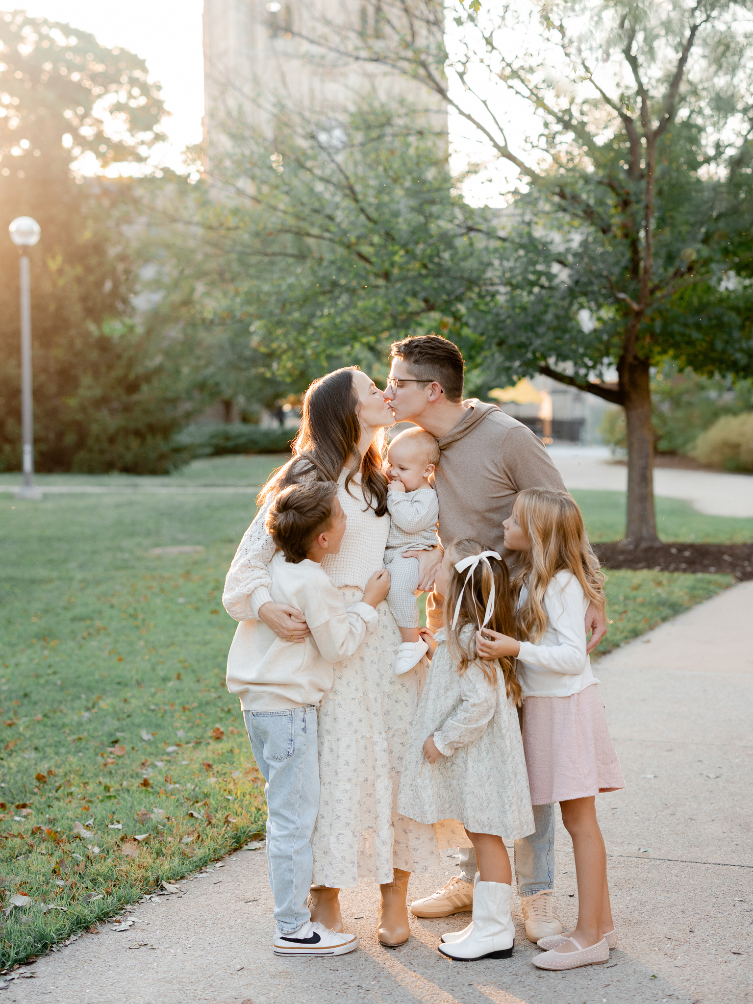 Parents share a kiss while children gather around them at sunset in Columbia, MO, photographed by Columbia Missouri family photographer.